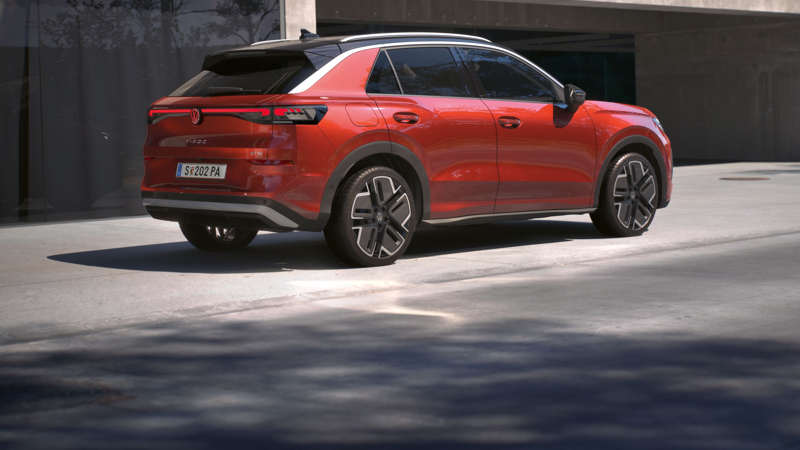 Uma vista traseira de 3/4 de um Volkswagen T-Roc Style vermelho, estacionado à frente de um edifício.