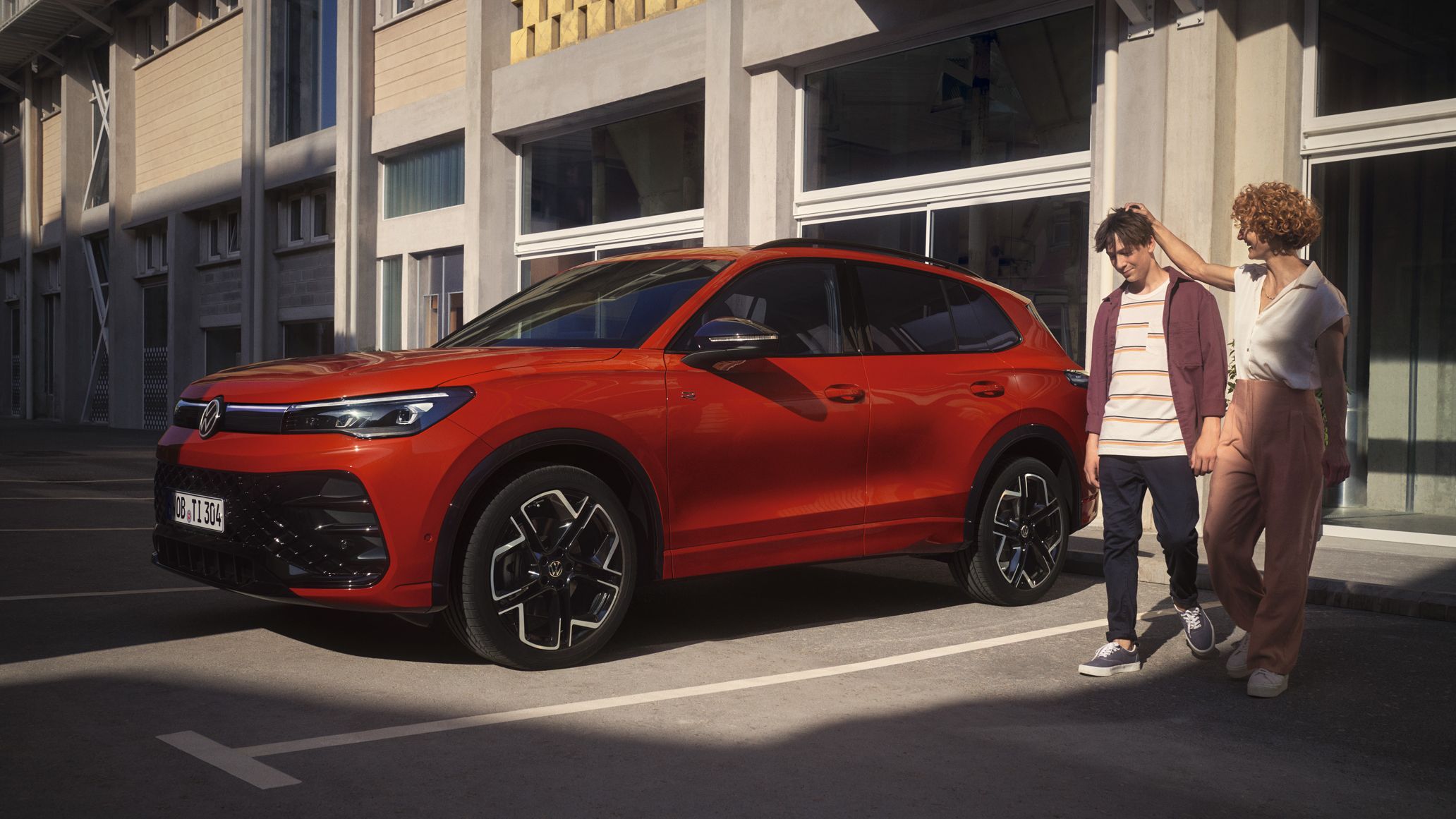 VW Tiguan vermelho estacionado em frente a um edifício, com uma mulher e um adolescente a caminharem ao lado.