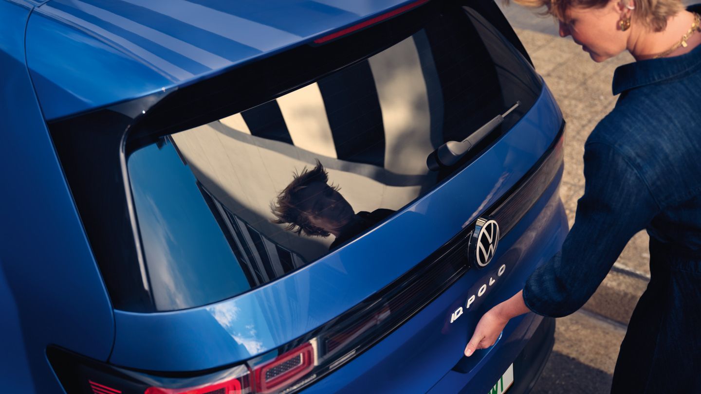 Eine Frau öffnet die Kofferraumklappe eines blauen VW ID. Polo Style.