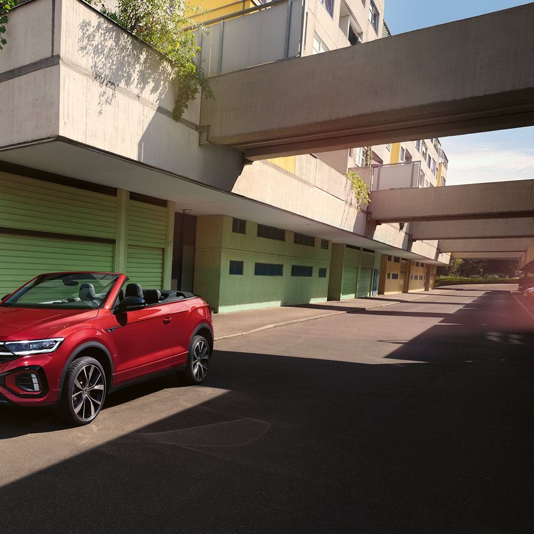 VW T-Roc Cabrio vermelho com a capota aberta, estacionado à beira da estrada. Uma mulher com dois cães está ao lado.