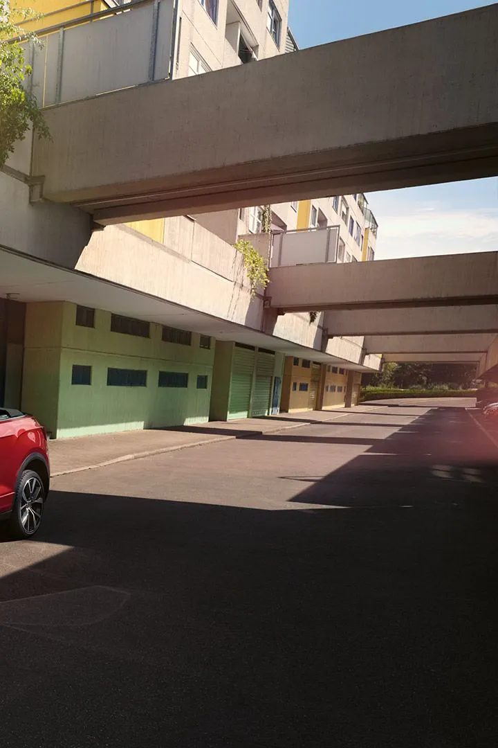 VW T-Roc Cabrio vermelho com a capota aberta, estacionado à beira da estrada. Uma mulher com dois cães está ao lado.