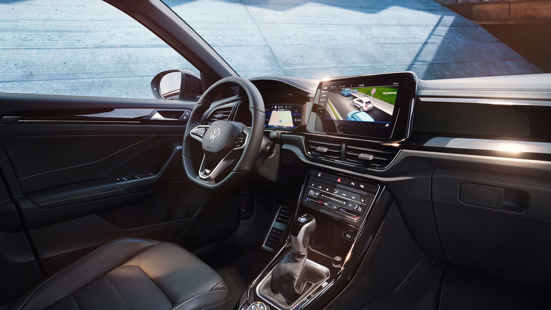 Interior do VW T-Roc, vista do lugar do passageiro para o lugar do condutor e cockpit com volante multifunções e sistema Infotainment