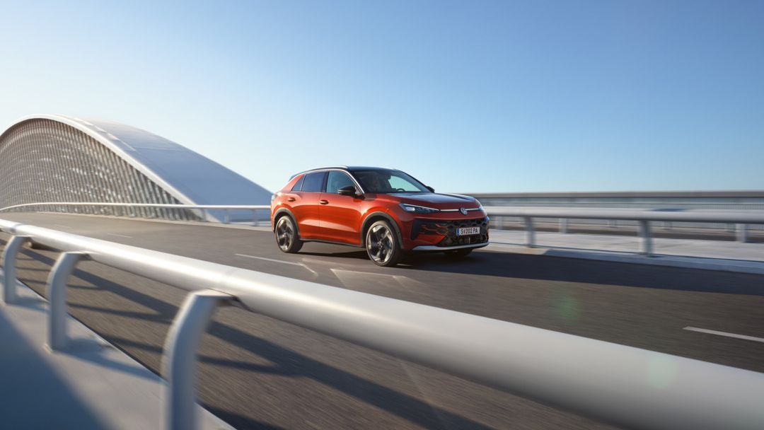 Um VW T-Roc Style vermelho circula numa ponte moderna com arquitetura curvilínea.