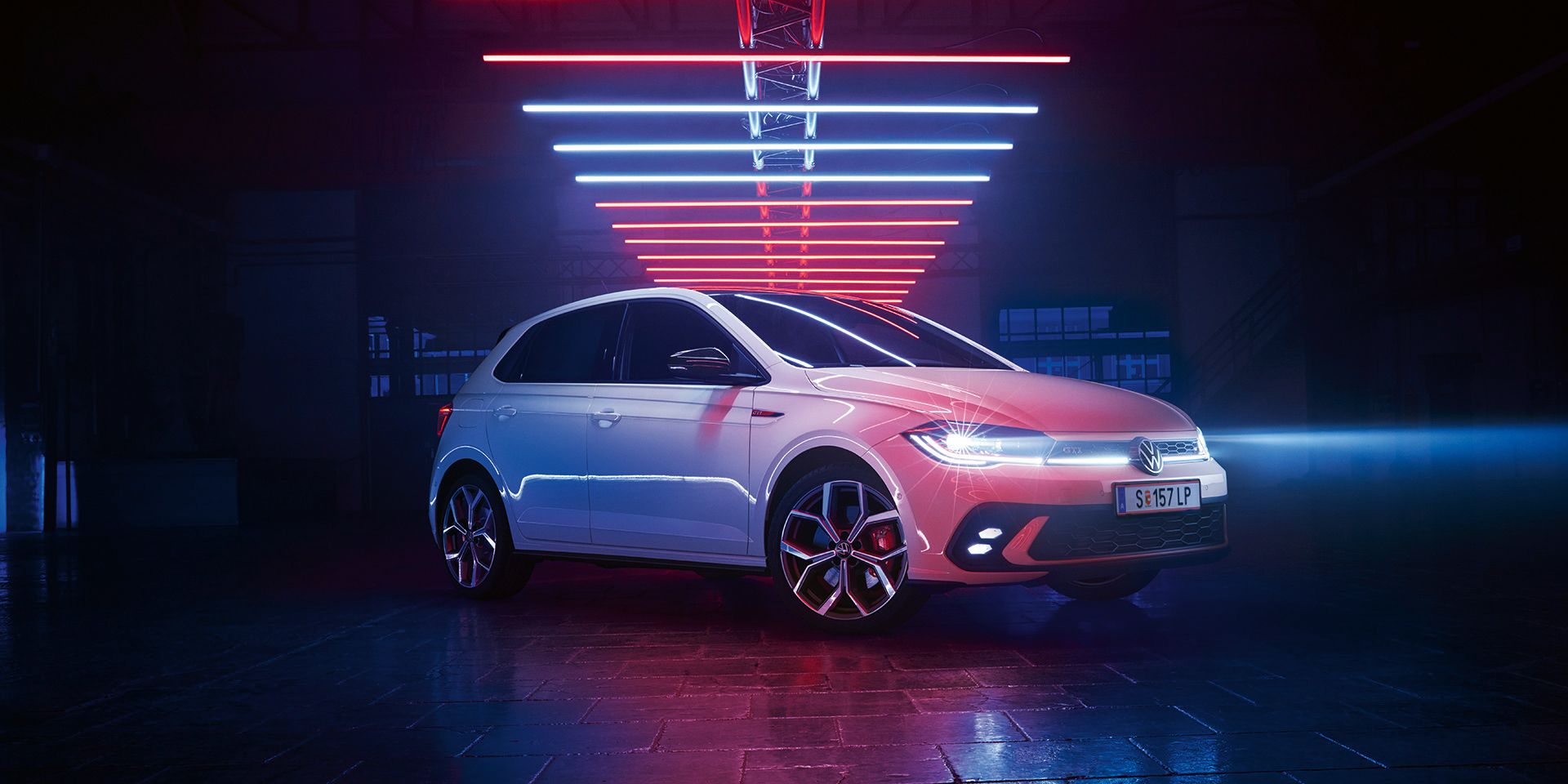 Fotografia de um VW Polo GTI branco, num salão escuro, com os faróis LED ligados, sob elementos luminosos.
