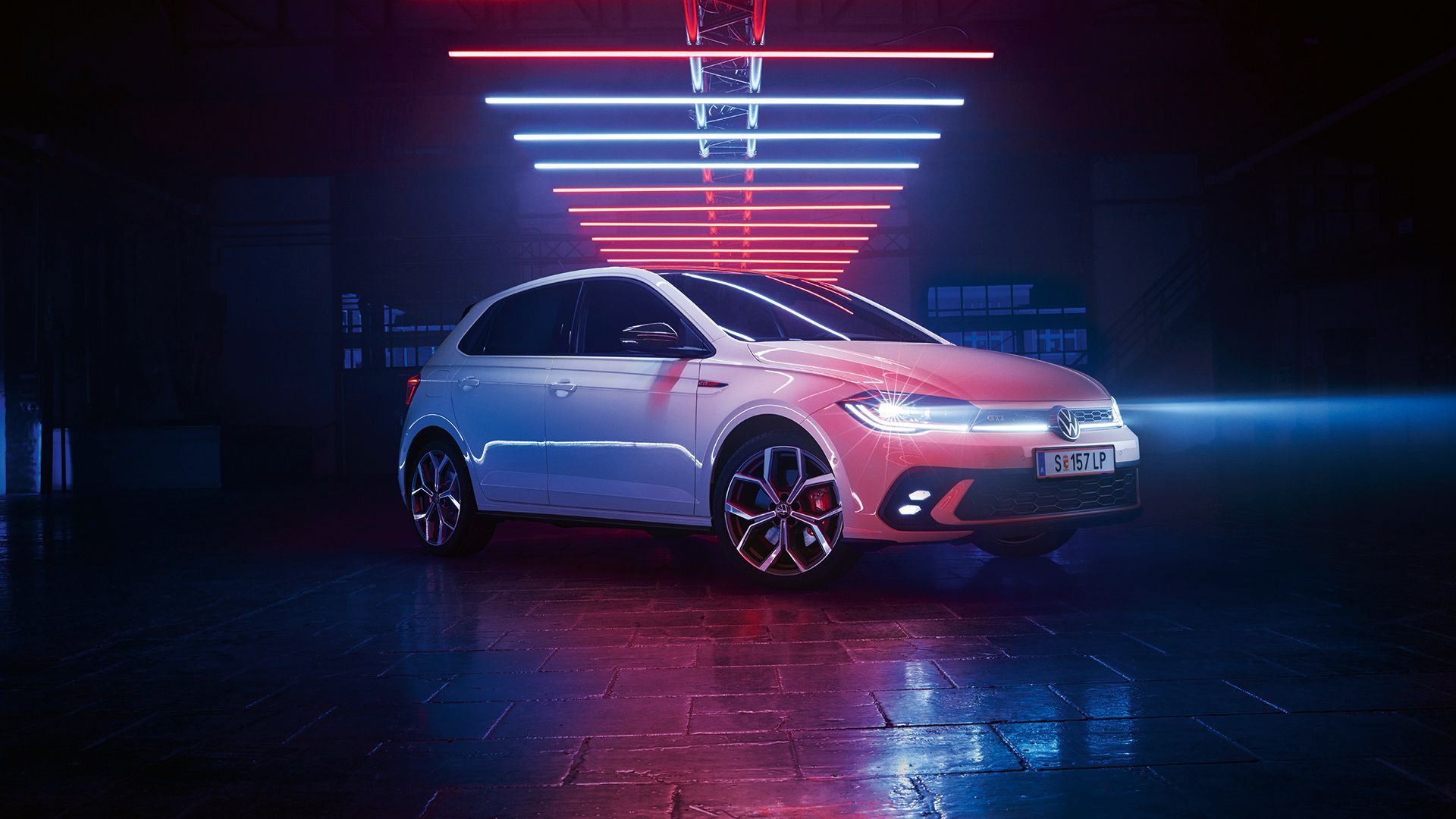 Fotografia de um VW Polo GTI branco, num salão escuro, com os faróis LED ligados, sob elementos luminosos.