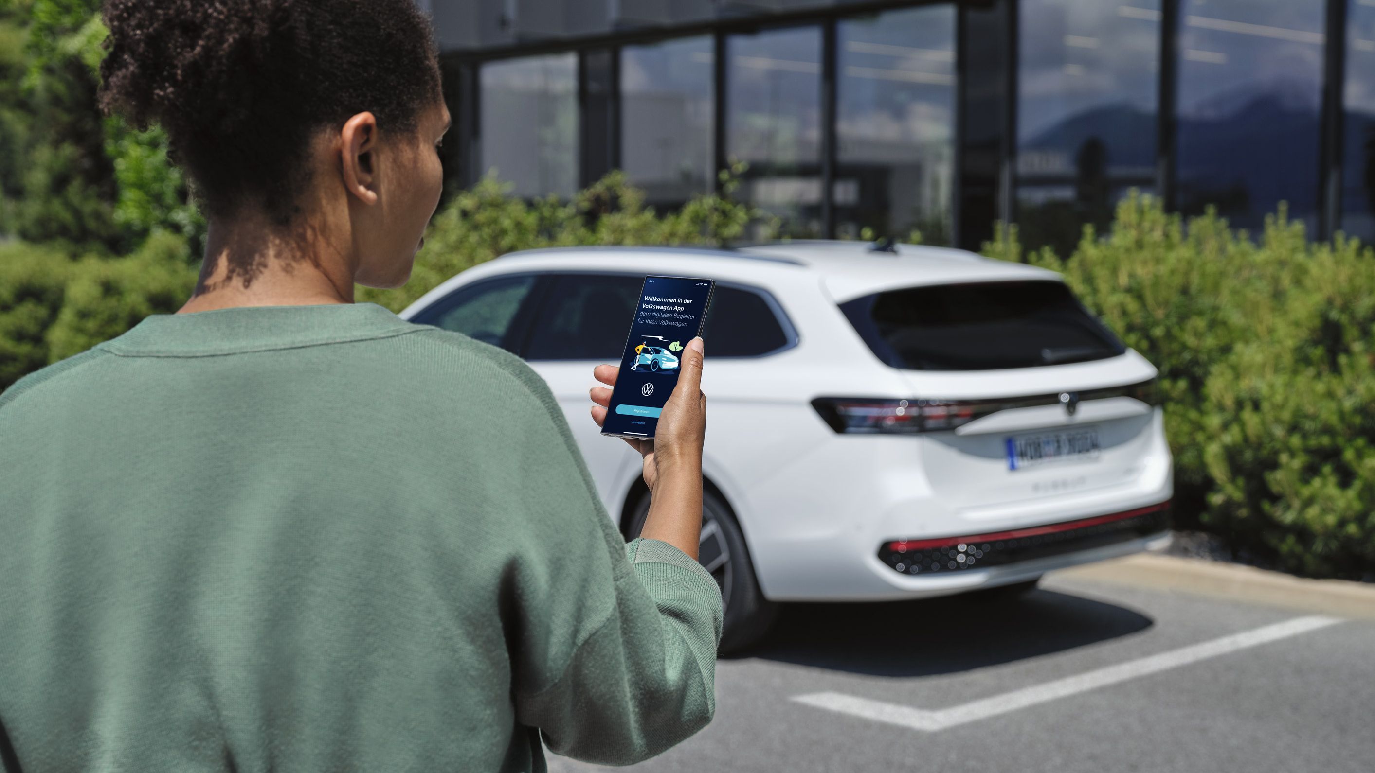 VW Passat branco estacionado à frente de um edifício. Uma mulher vista de trás a olhar para o seu smartphone.