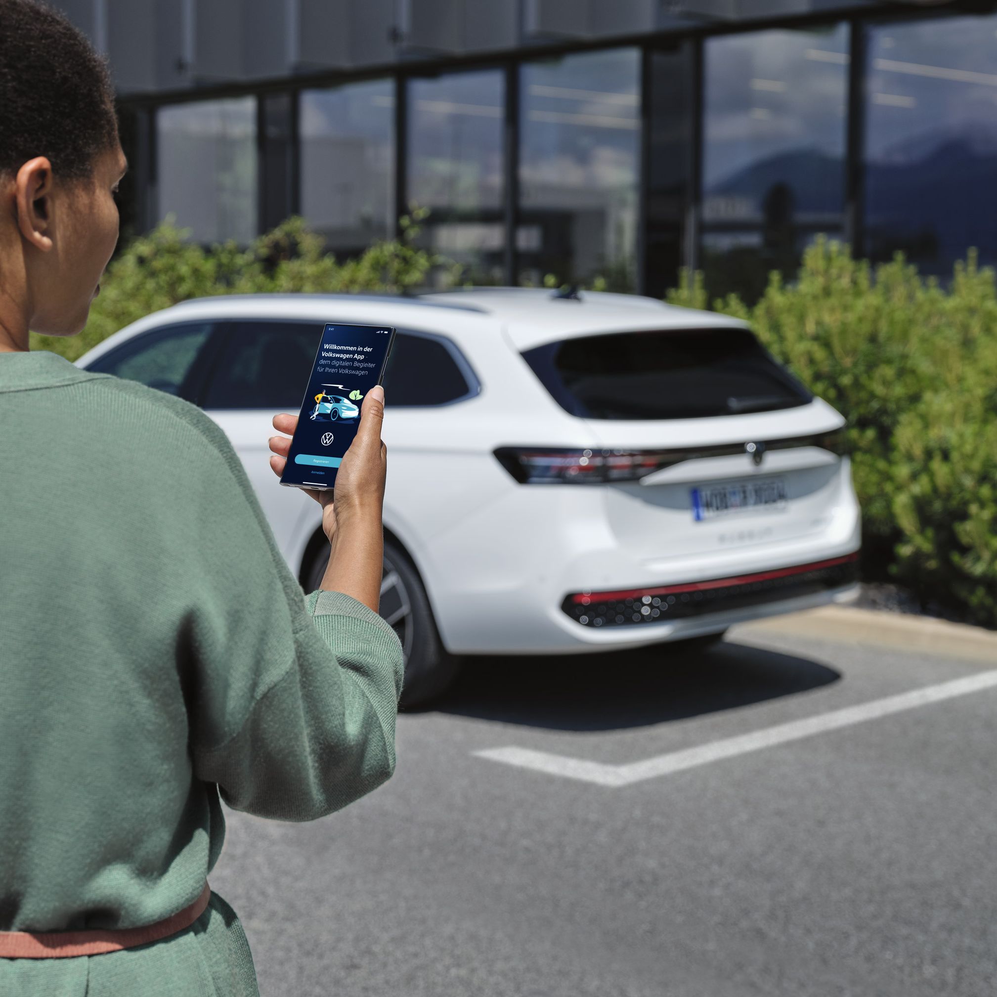 VW Passat branco estacionado à frente de um edifício. Uma mulher vista de trás a olhar para o seu smartphone.