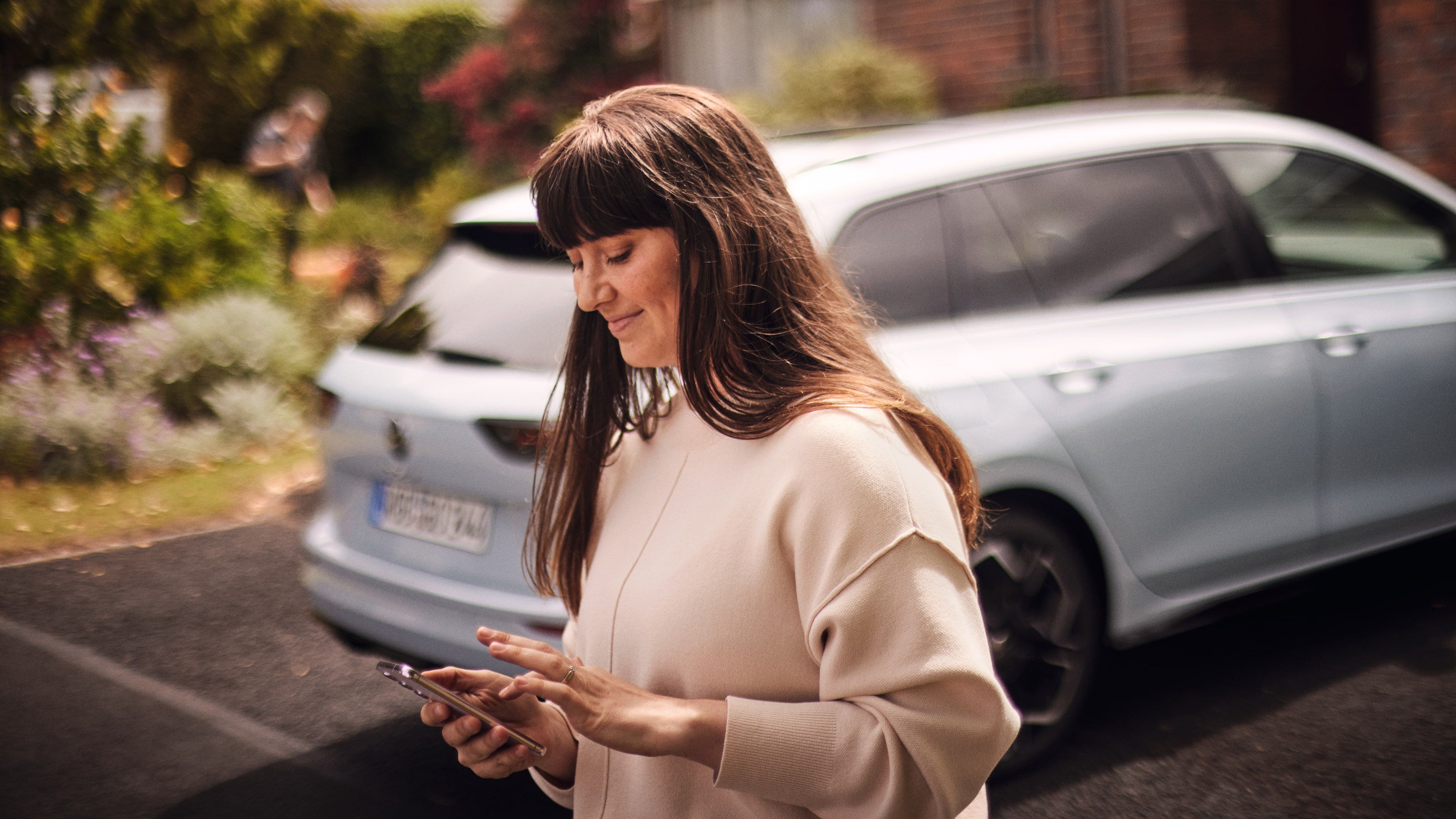 Uma mulher ao lado do seu VW Golf, a utilizar a Volkswagen App no seu smartphone.