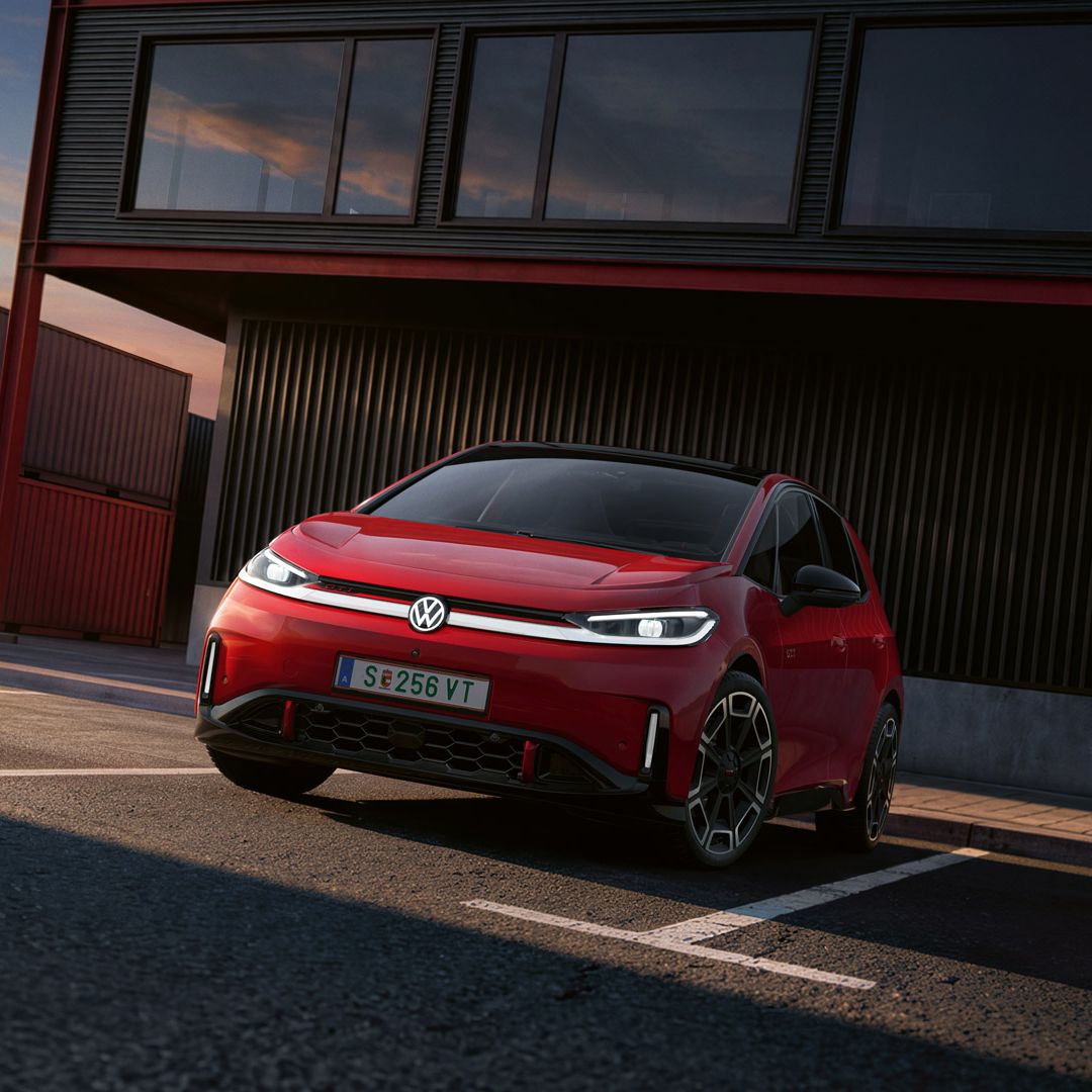 [AI-modified] – Vista frontal de um VW ID.3 GTI vermelho em frente a um edifício com os faróis ligados e o logótipo iluminado.
