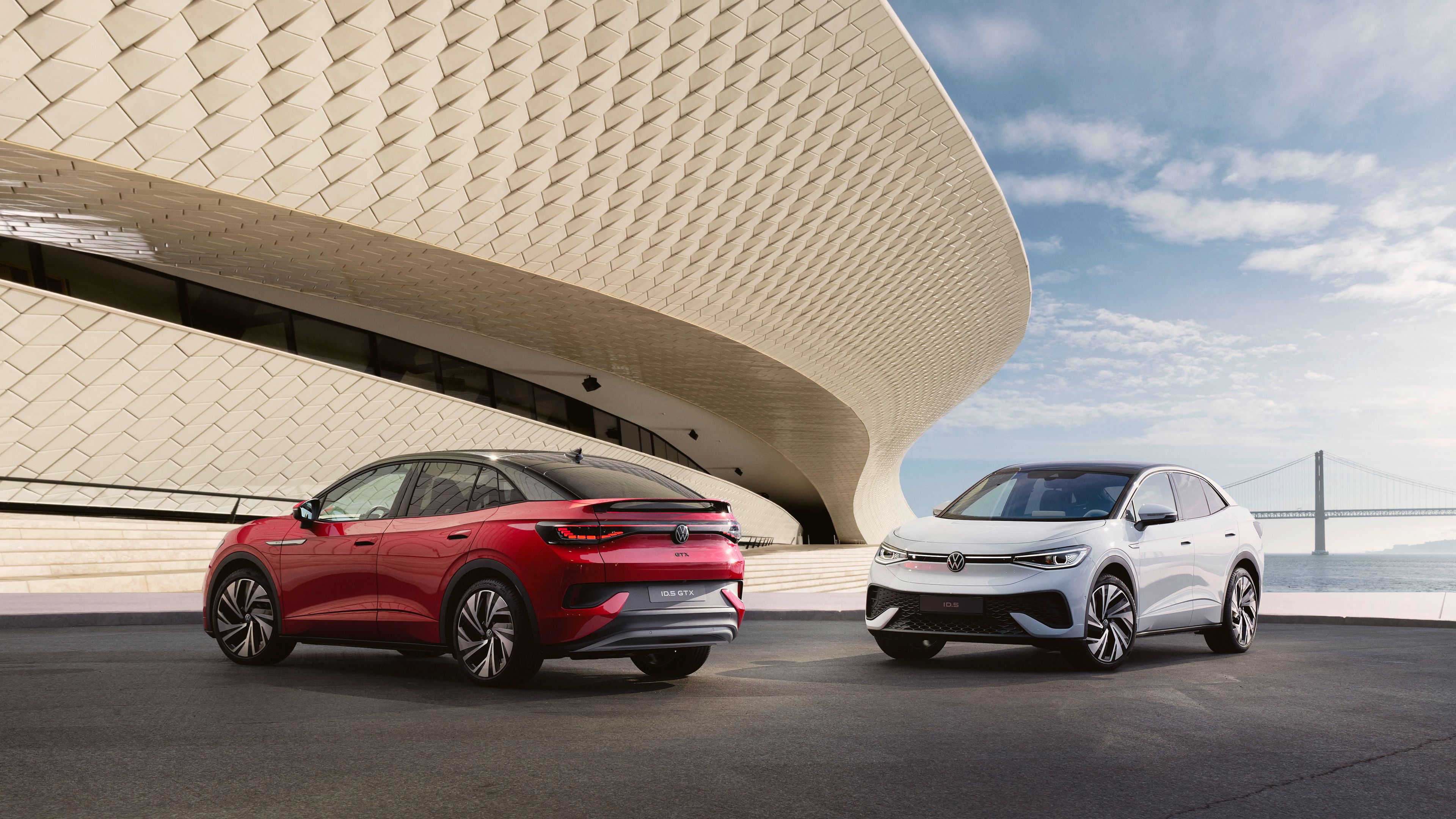 O Volkswagen ID.5 em cinzento e o ID.5 GTX em vermelho numa plataforma panorâmica. Em segundo plano paredes e céu azul com nuvens.
