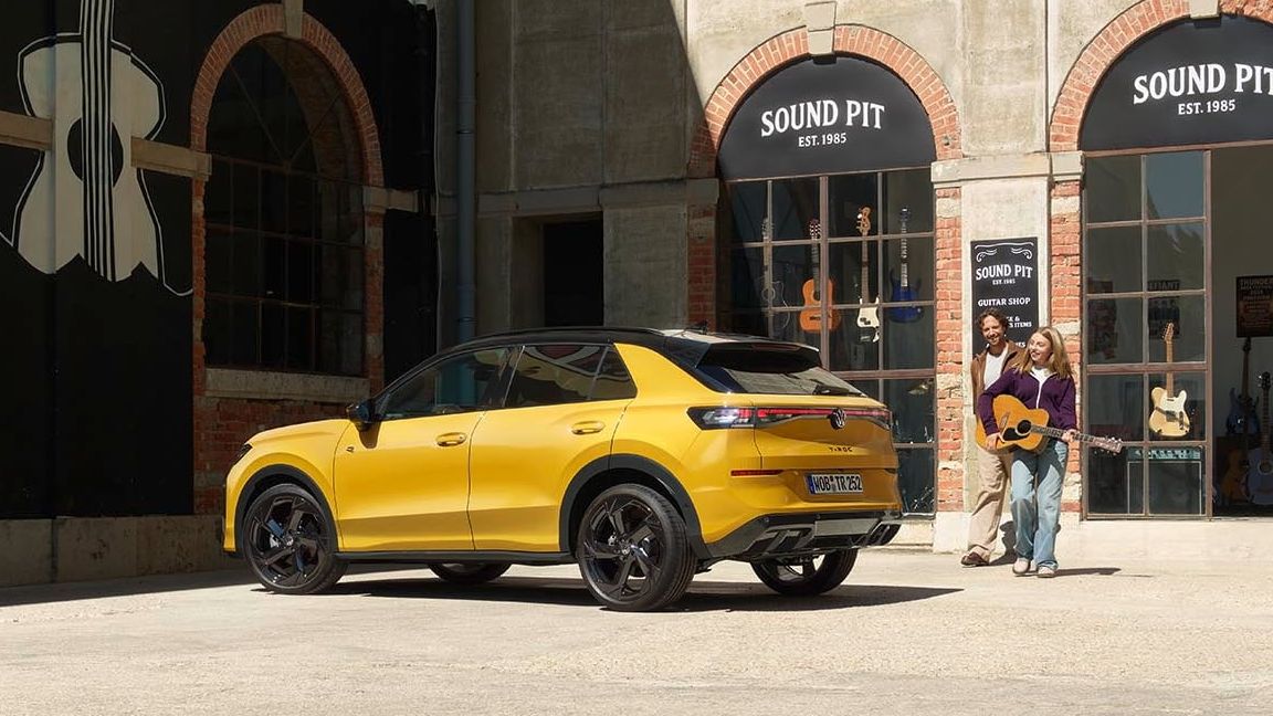 Pai e filha com uma guitarra junto de um VW T-Roc R-Line amarelo estacionado em frente a uma loja de música.