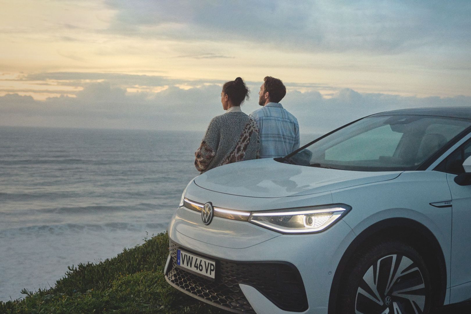 Volkswagen estacionado à beira de uma ravina e duas pessoas encostadas ao veículo a ver a vista