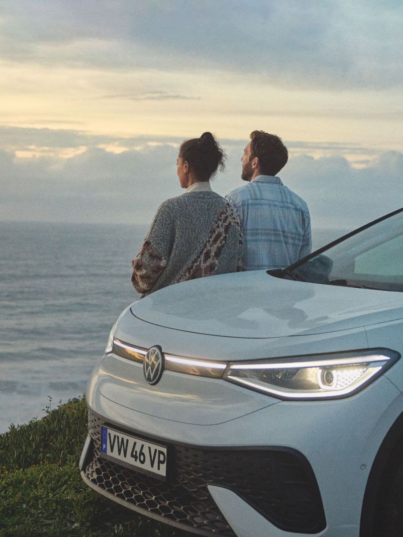 Volkswagen estacionado à beira de uma ravina e duas pessoas encostadas ao veículo a ver a vista
