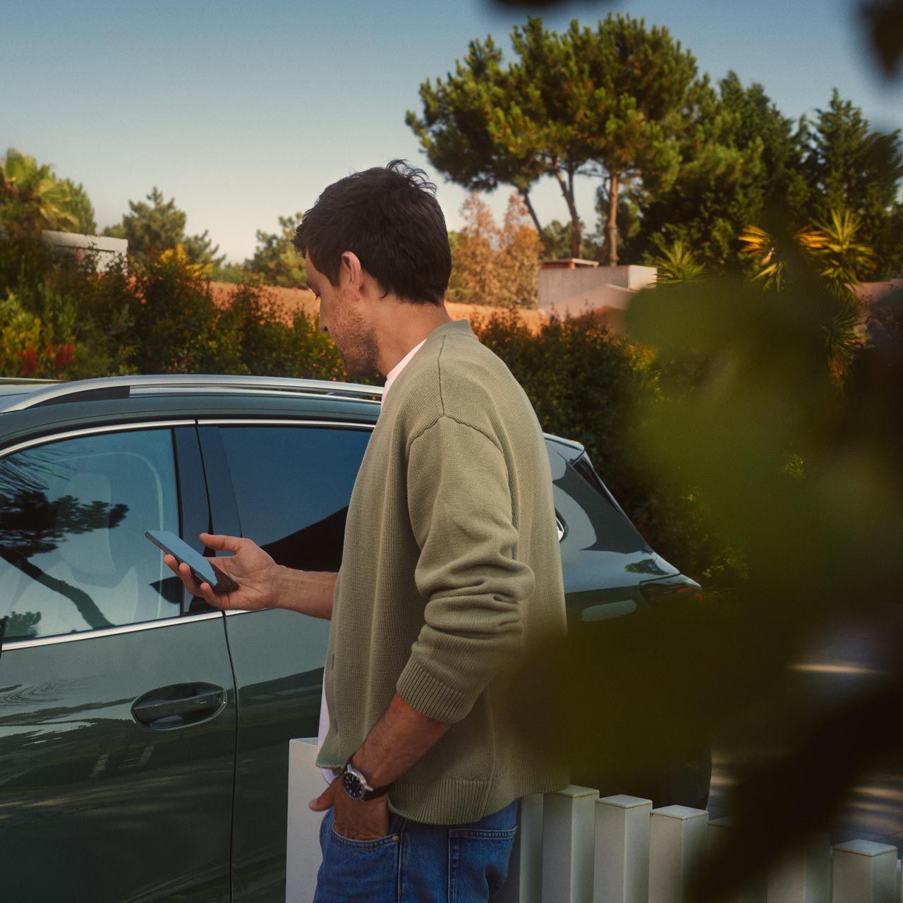 Um jovem no lado do condutor do VW Tiguan verde escuro opera o Park Assist Plus opcional através do seu smartphone.