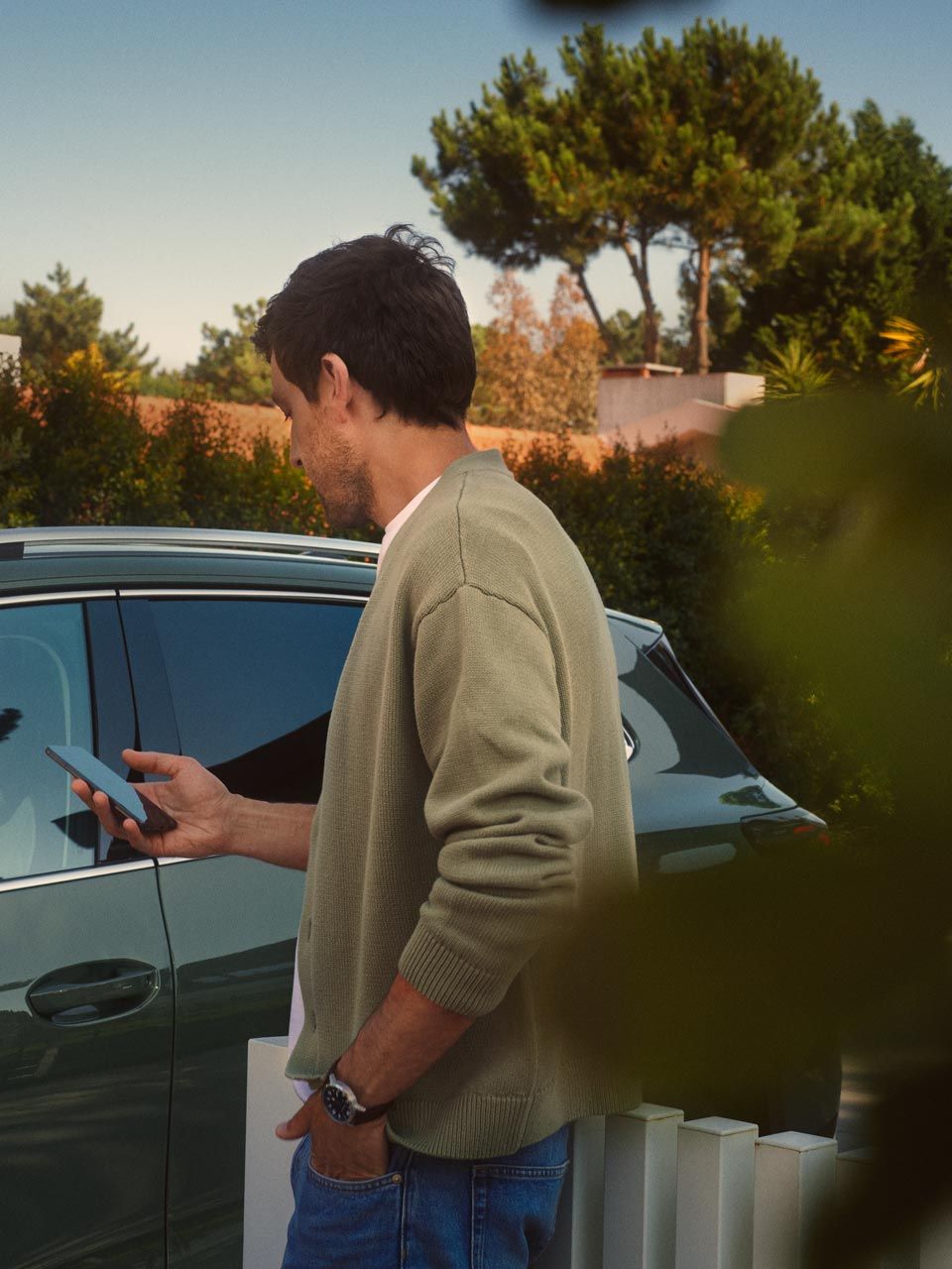 Um jovem no lado do condutor do VW Tiguan verde escuro opera o Park Assist Plus opcional através do seu smartphone.