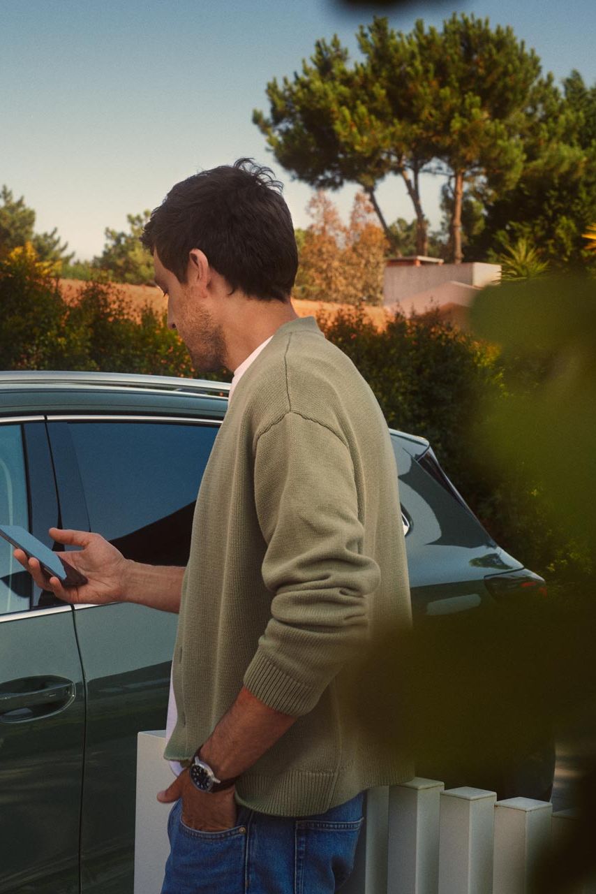 Um jovem no lado do condutor do VW Tiguan verde escuro opera o Park Assist Plus opcional através do seu smartphone.
