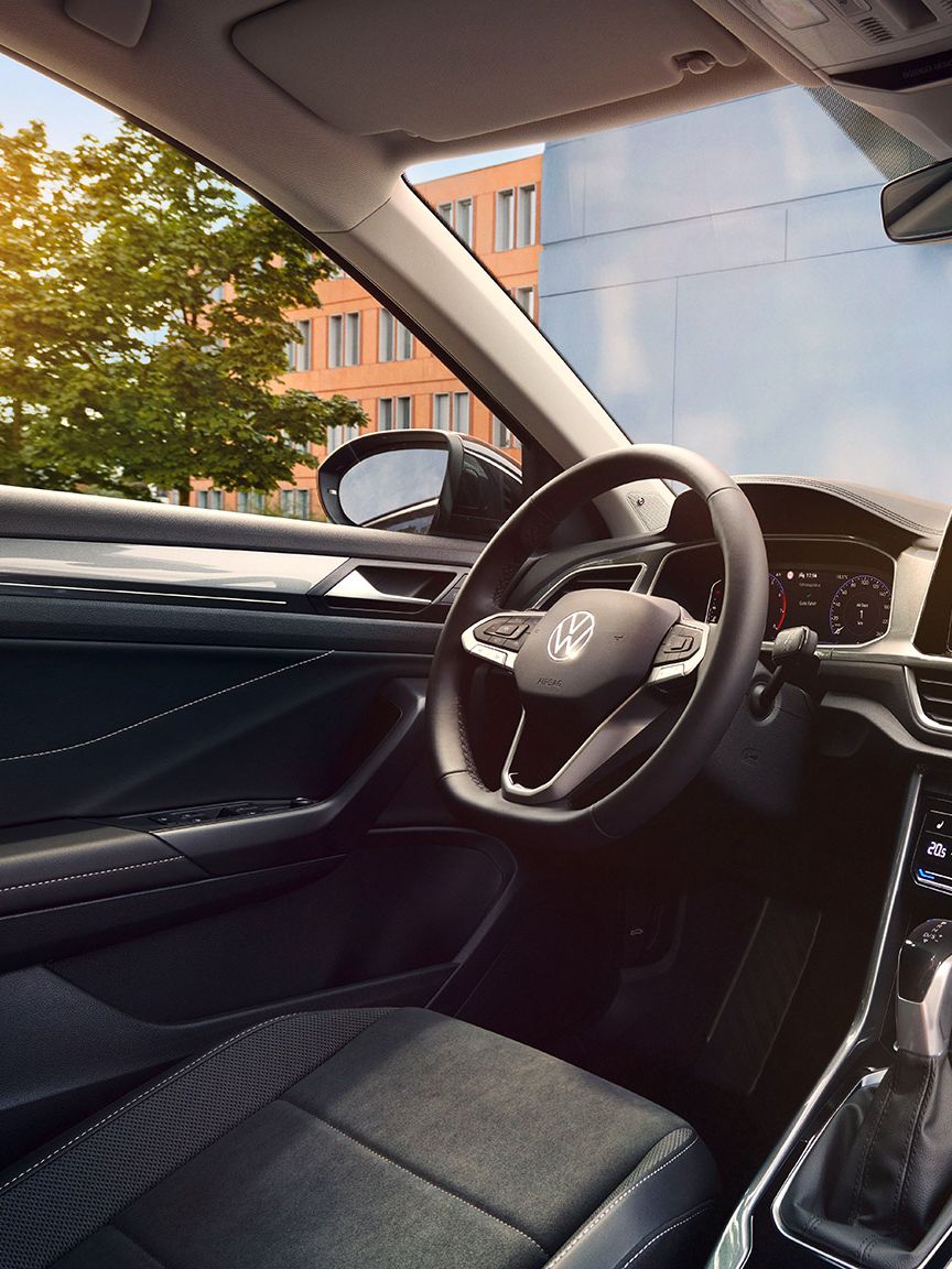Interior do VW T-Roc, vista do lugar do passageiro para o lugar do condutor e cockpit com volante multifunções e sistema Infotainment