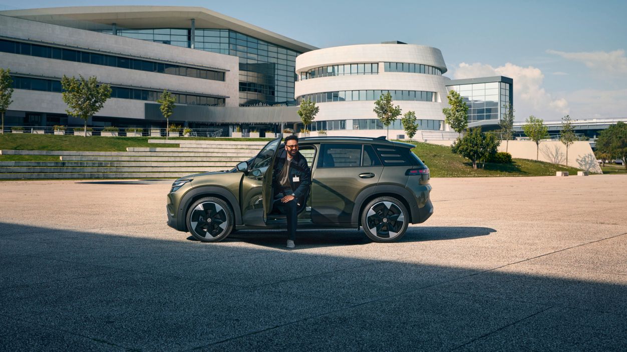Um homem sai pela porta do condutor num VW ID. Cross perante um edifício empresarial moderno com vários andares.