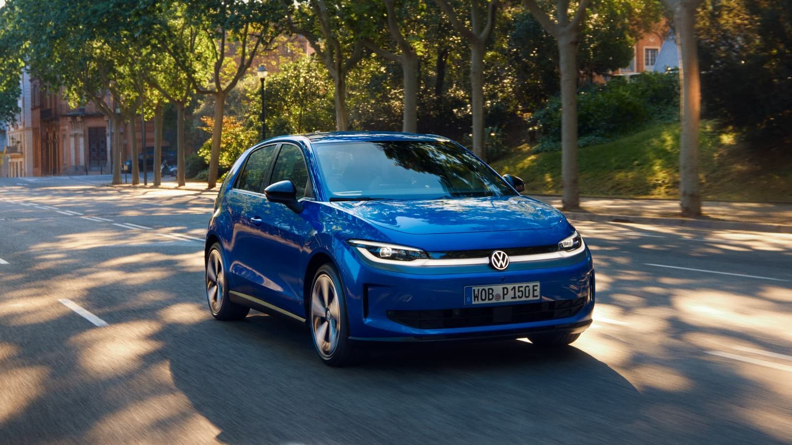 Um VW ID. Polo circula por uma estrada larga, sob a sombra de uma rua arborizada.