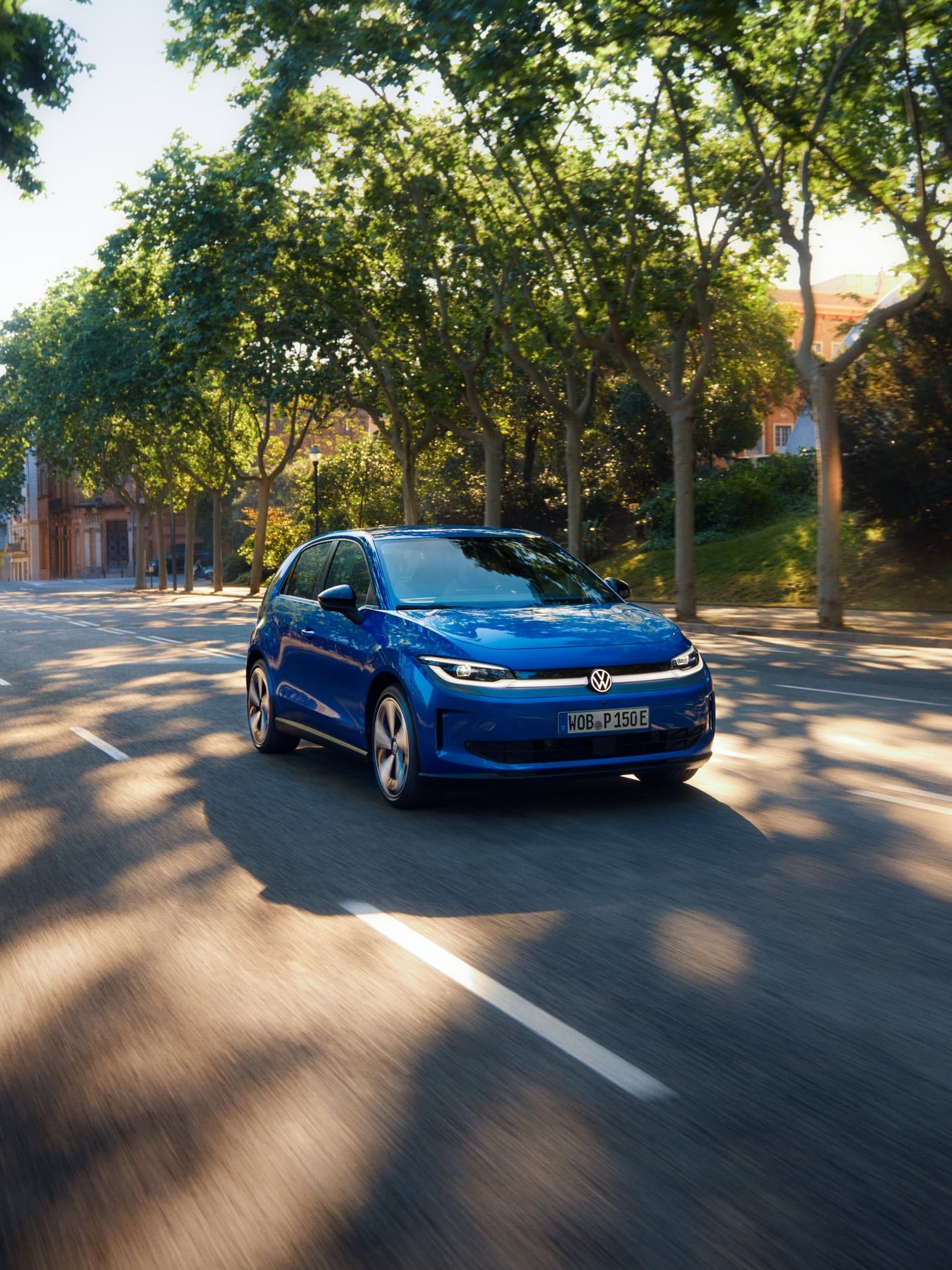 Um VW ID. Polo circula por uma estrada larga, sob a sombra de uma rua arborizada.