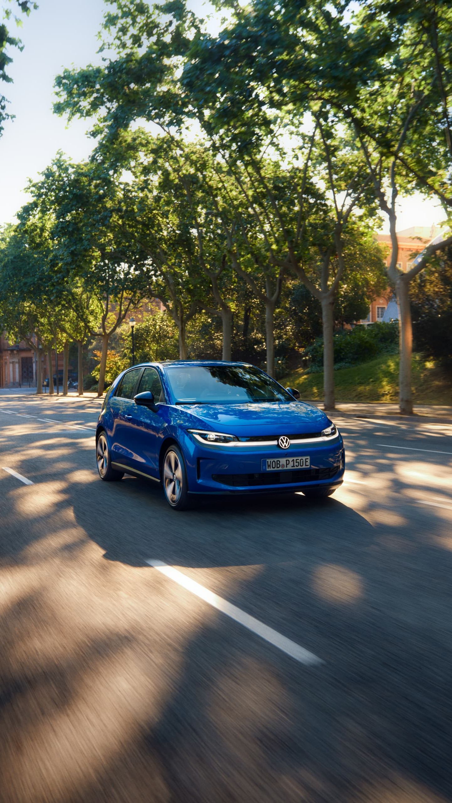 Um VW ID. Polo circula por uma estrada larga, sob a sombra de uma rua arborizada.