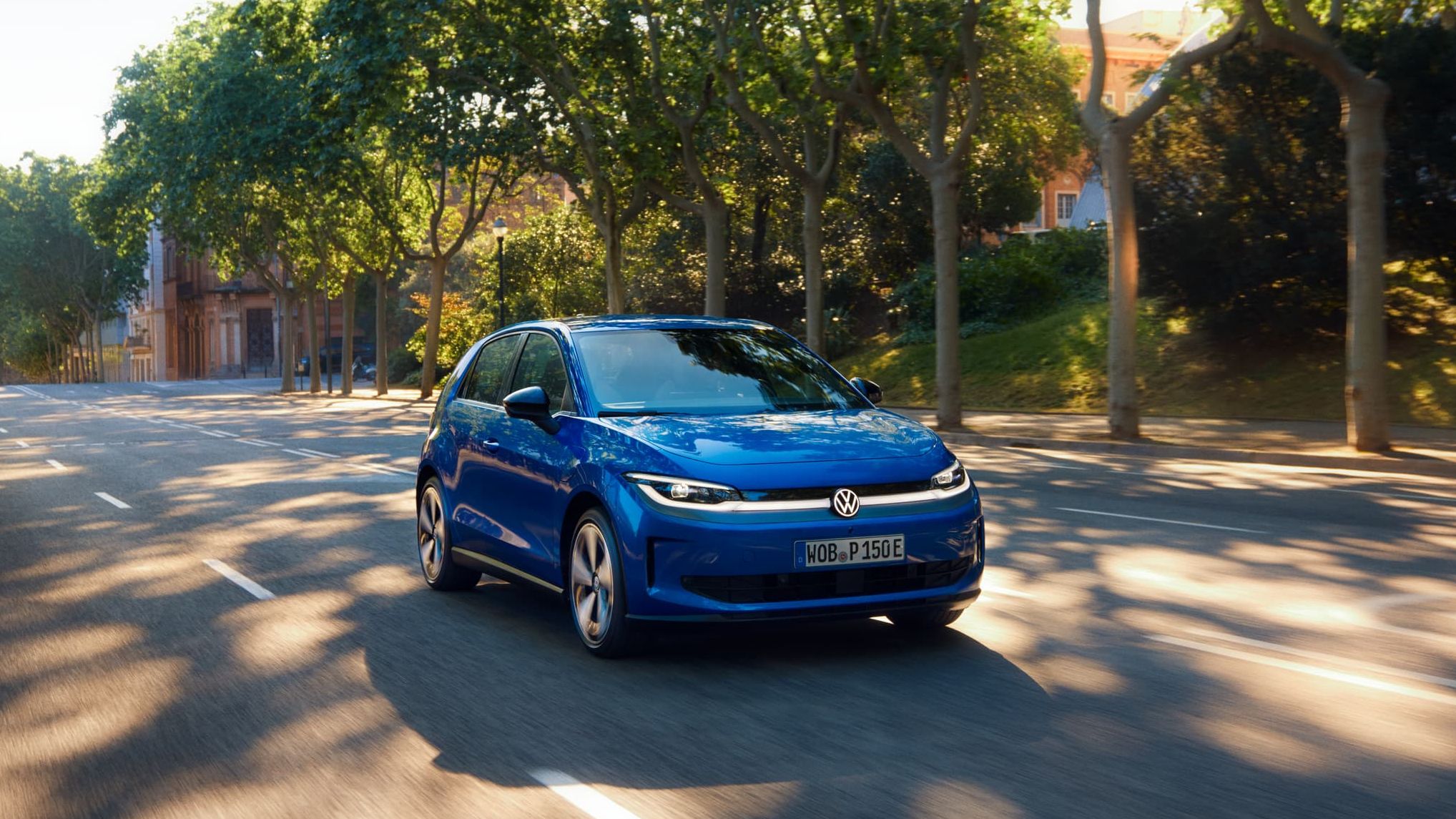 Um VW ID. Polo circula por uma estrada larga, sob a sombra de uma rua arborizada.
