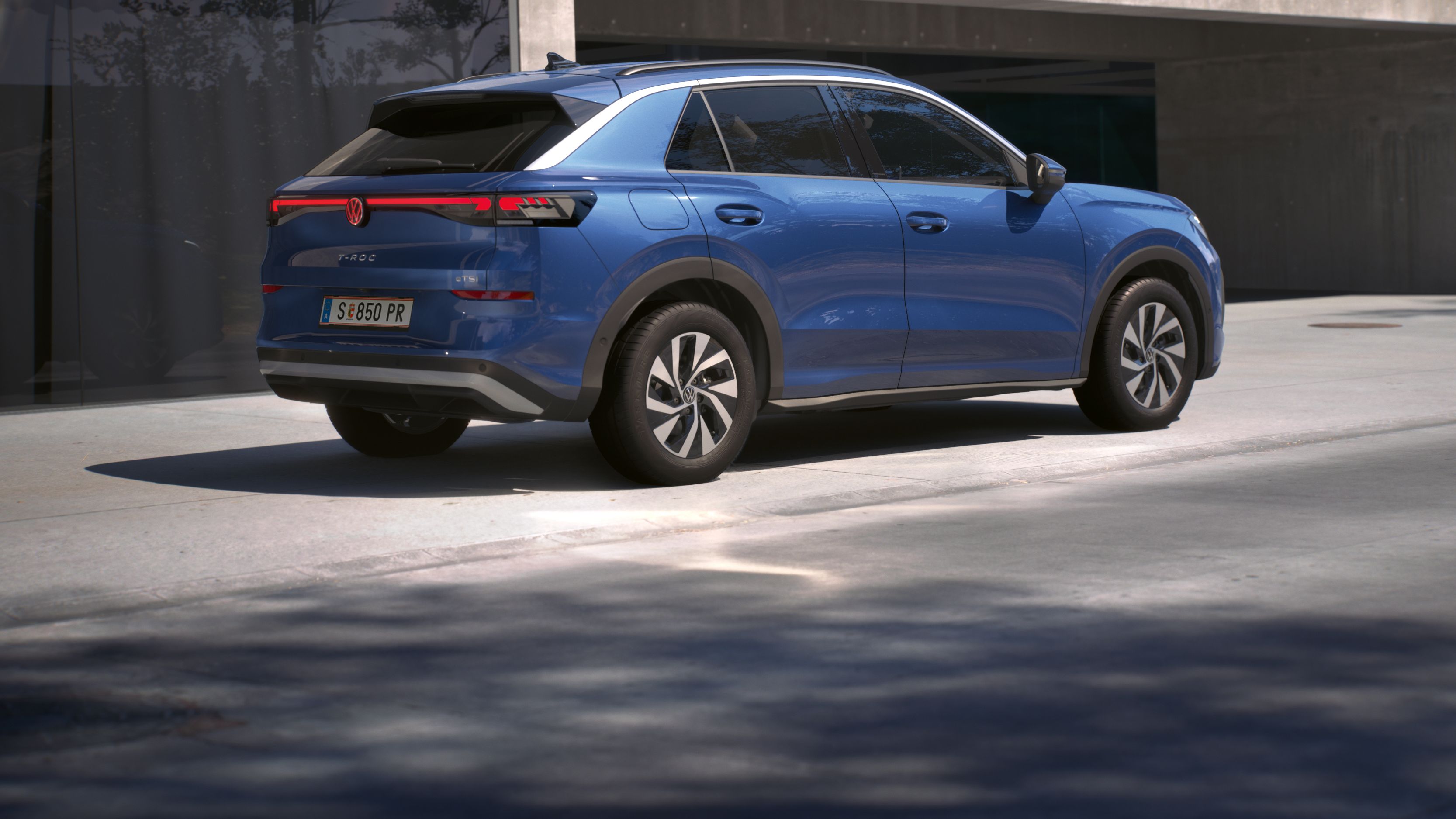 Uma vista traseira de 3/4 de um Volkswagen T-Roc Life azul, estacionado à frente de um edifício.