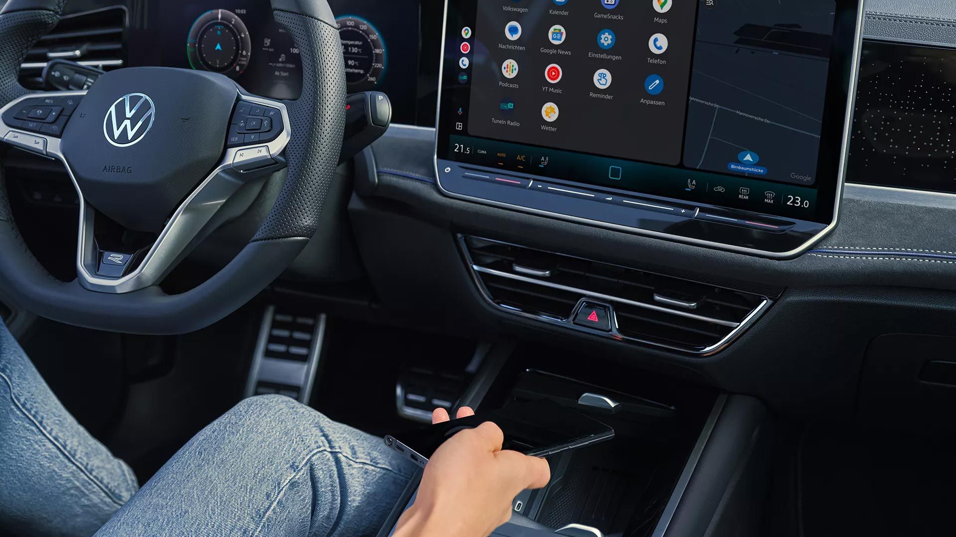 Vista detalhada do cockpit do VW Passat. Uma pessoa no banco do condutor segura um smartphone na mão.