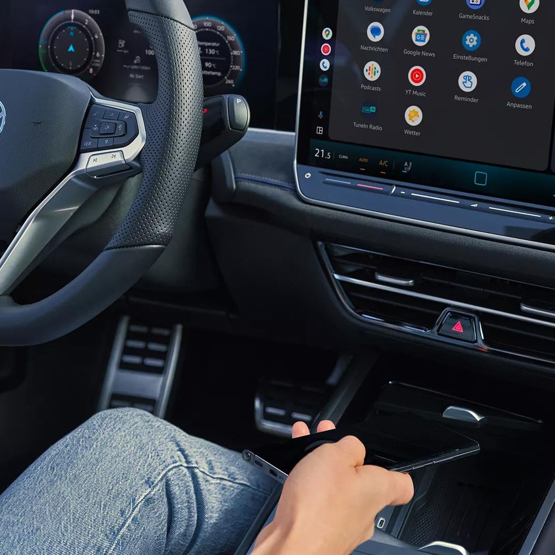 Vista detalhada do cockpit do VW Passat. Uma pessoa no banco do condutor segura um smartphone na mão.