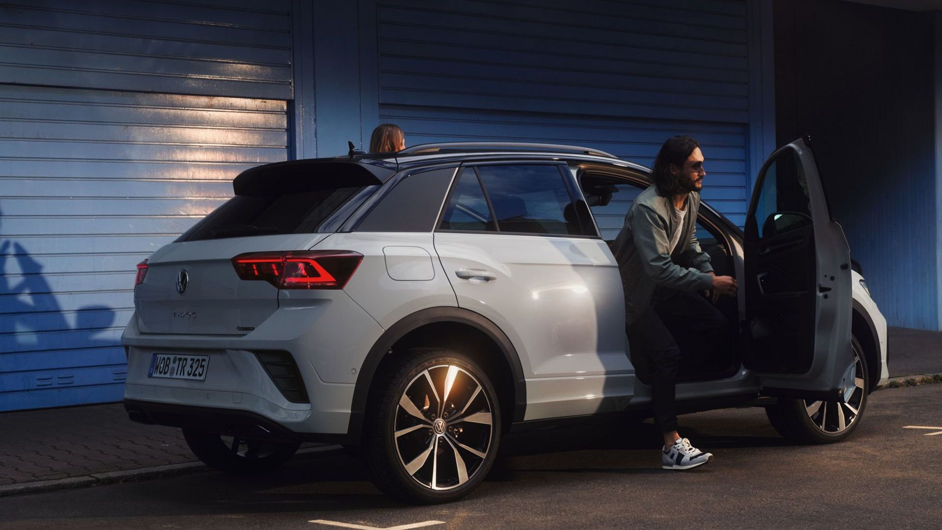 Um VW T-Roc branco parado à frente de um edifício. Vista da traseira e lateral.