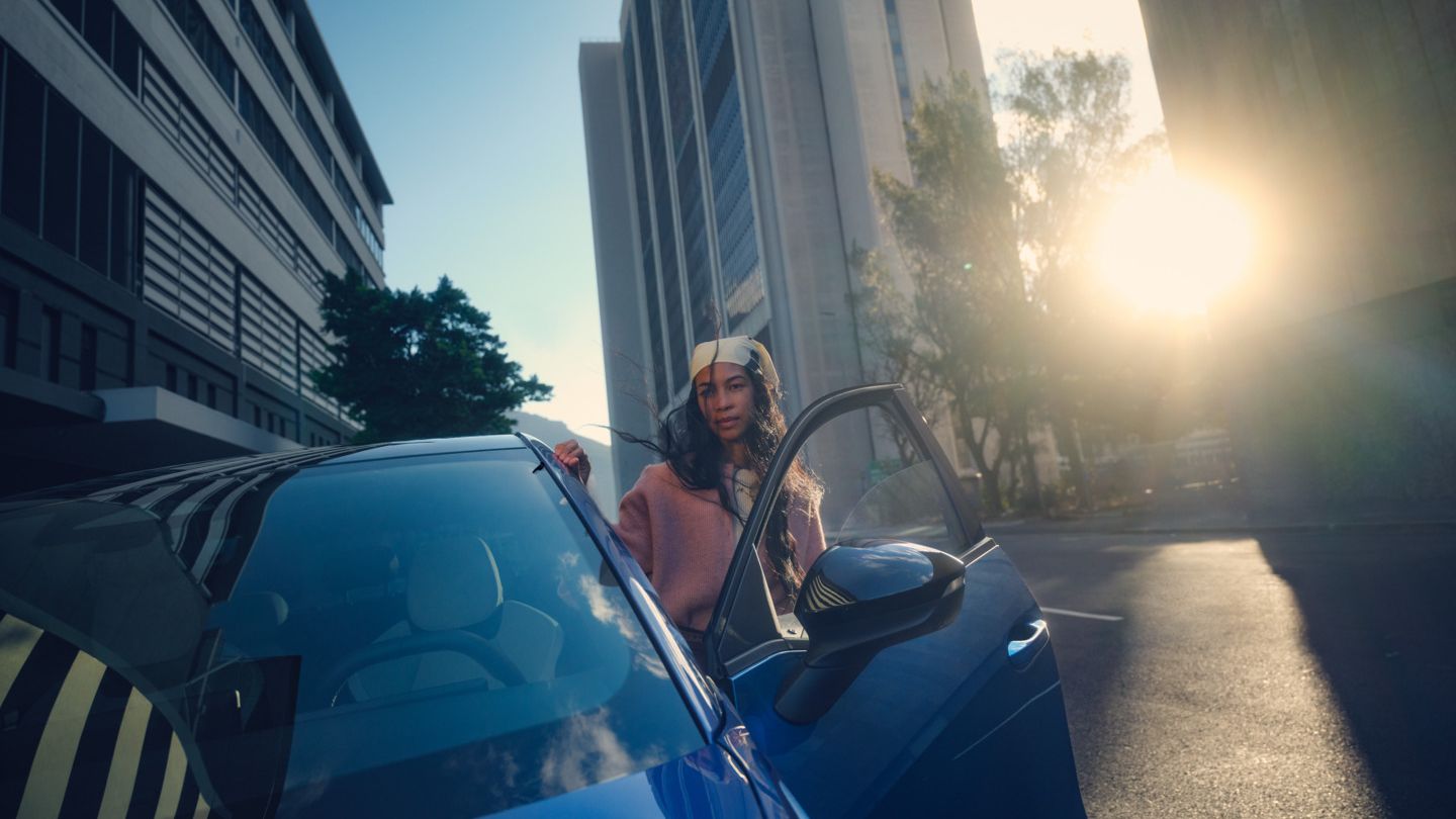 Um VW ID. Polo estacionado numa cidade ao pôr do sol, uma mulher sai do lado do condutor.