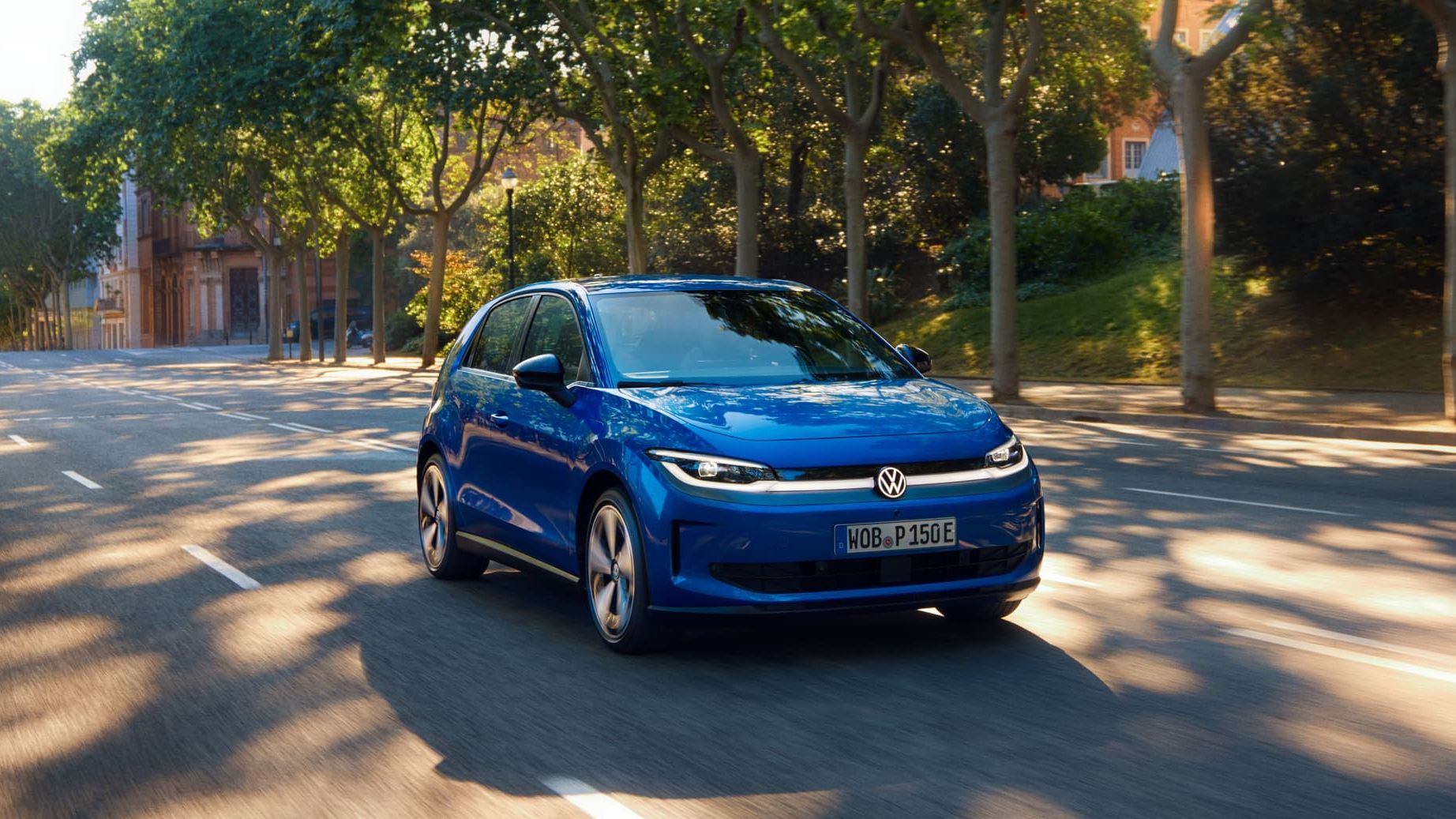 Um VW ID. Polo circula por uma estrada larga, sob a sombra de uma rua arborizada.