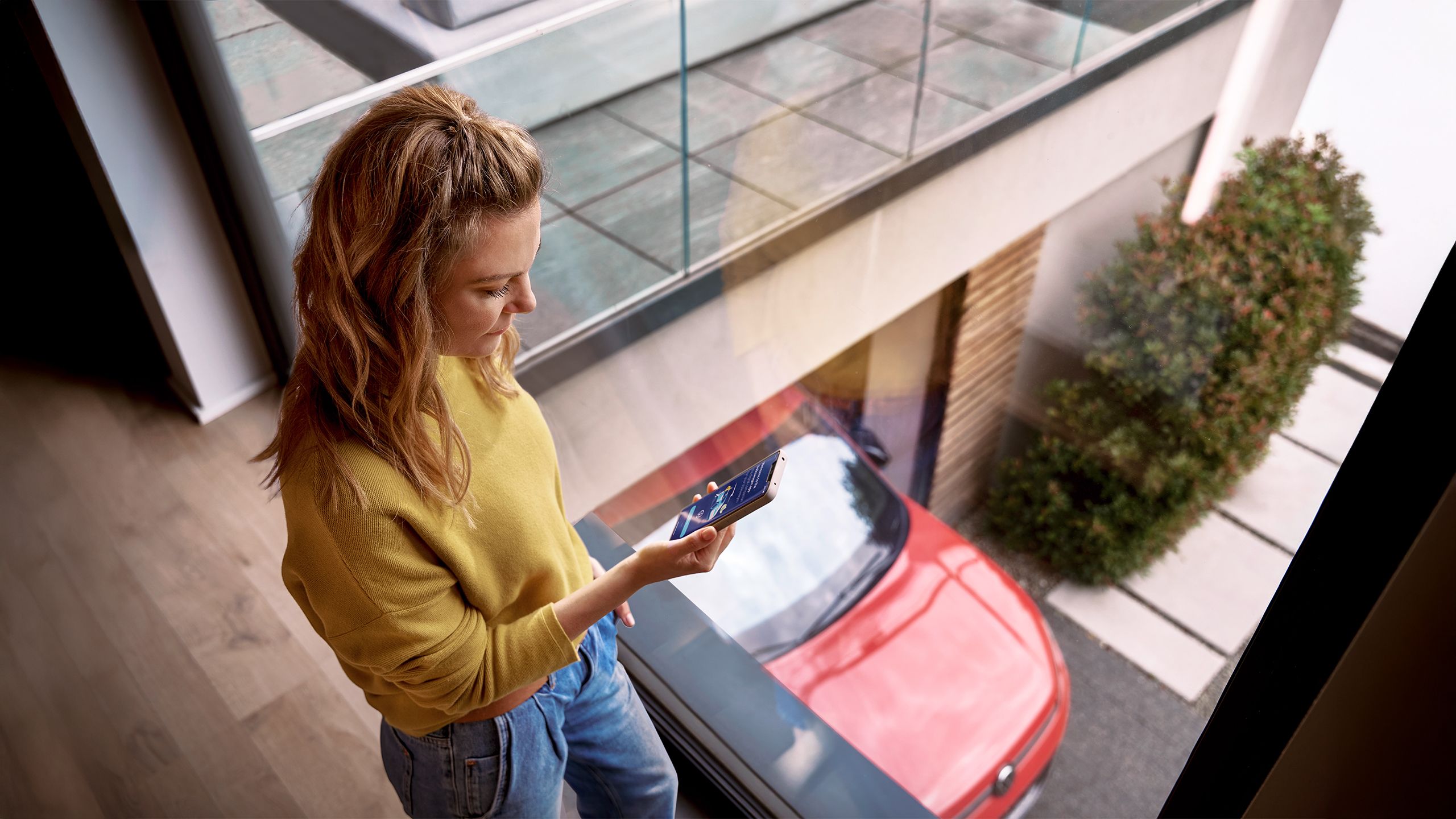 Mulher olha para o telemóvel. Em segundo plano um Volkswagen vermelho.