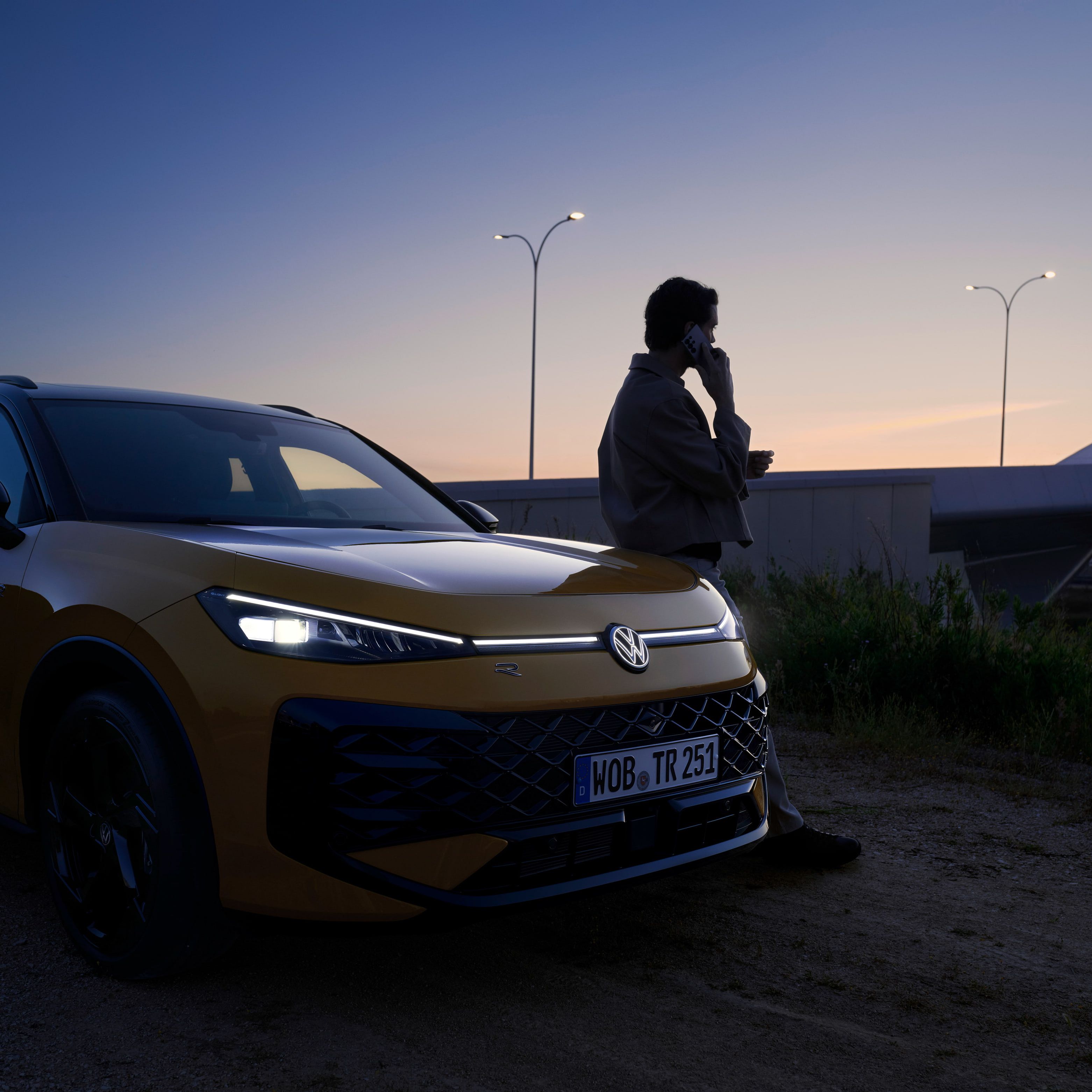 Um homem junto a um VW T-Roc R-Line com os faróis ligados e o logótipo iluminado.
