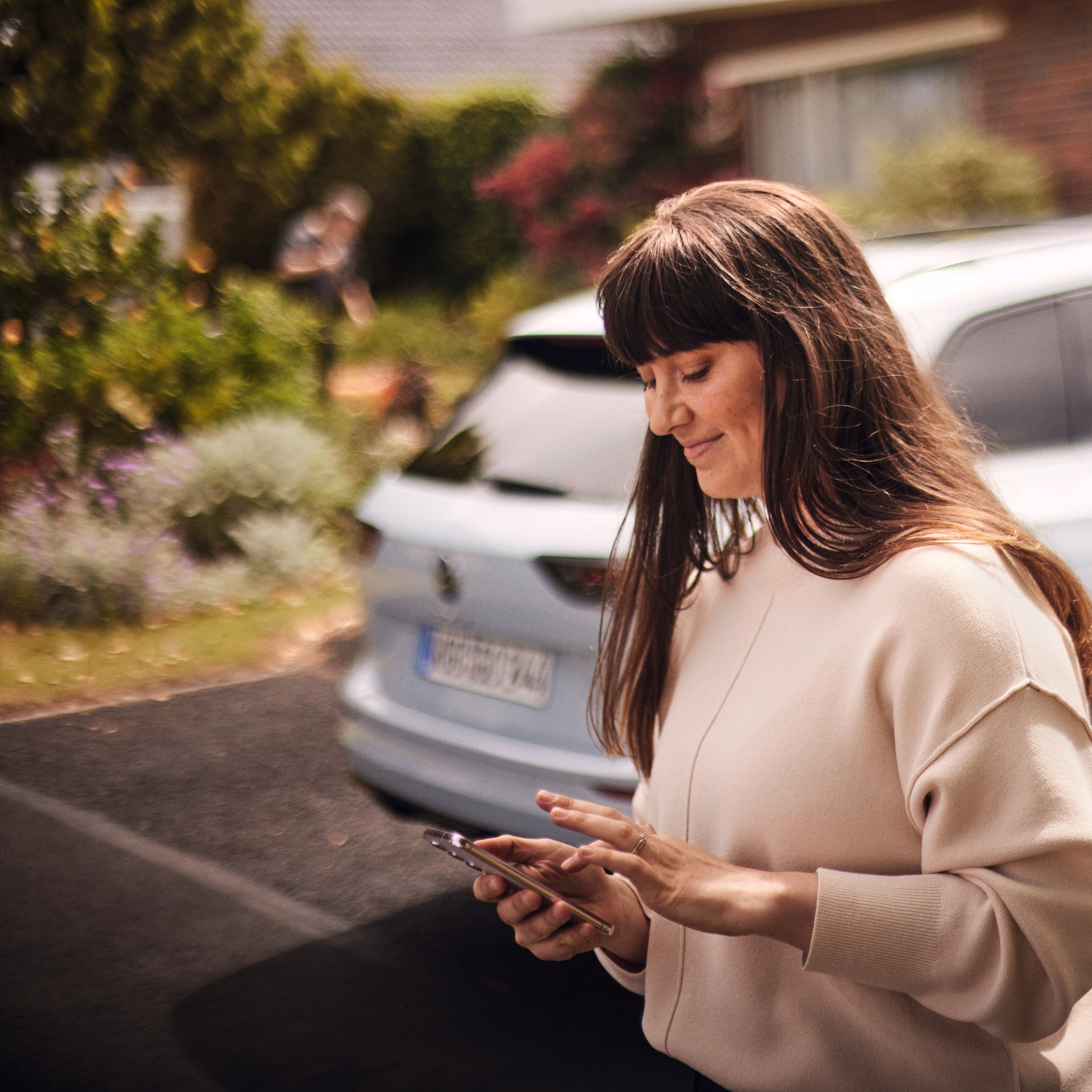 Uma mulher ao lado do seu VW Golf, a utilizar a Volkswagen App no seu smartphone.