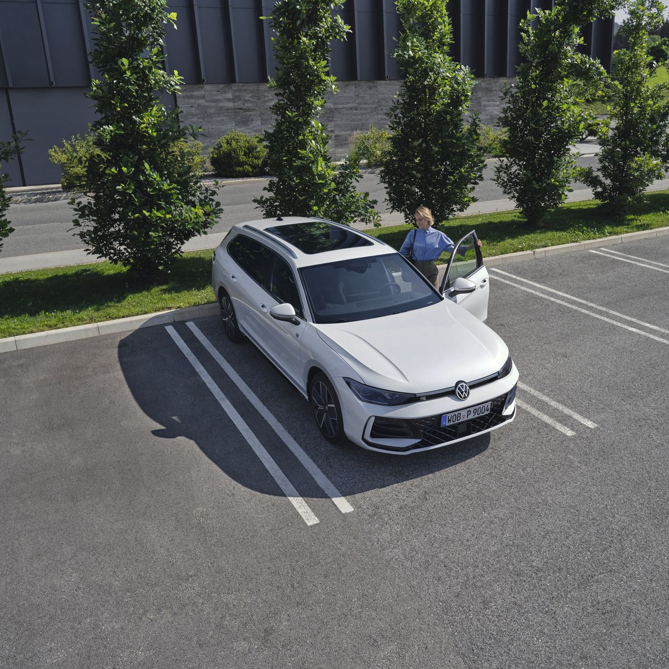 Fotografia de cima de um VW Passat branco num parque de estacionamento, uma mulher entra no lado do condutor.