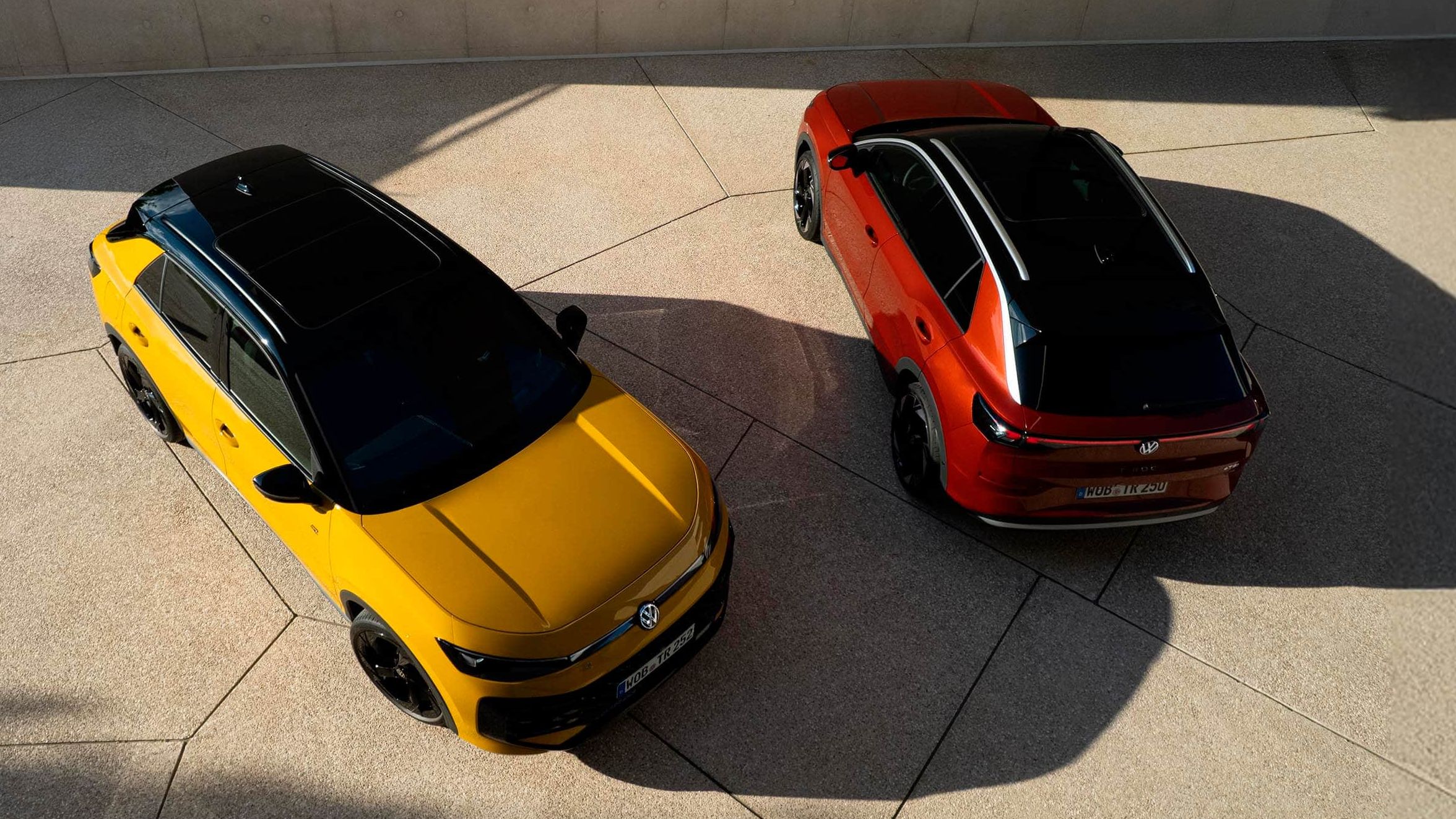 Um VW T-Roc R-Line amarelo e um VW T-Roc Style vermelho vistos de cima em perspetiva oblíqua em frente a um edifício moderno.