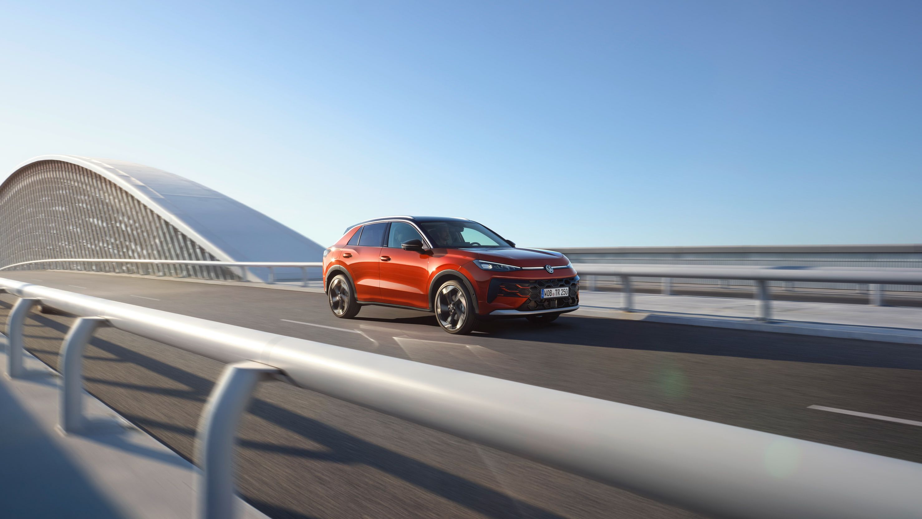 Um VW T-Roc Style vermelho circula numa ponte moderna.