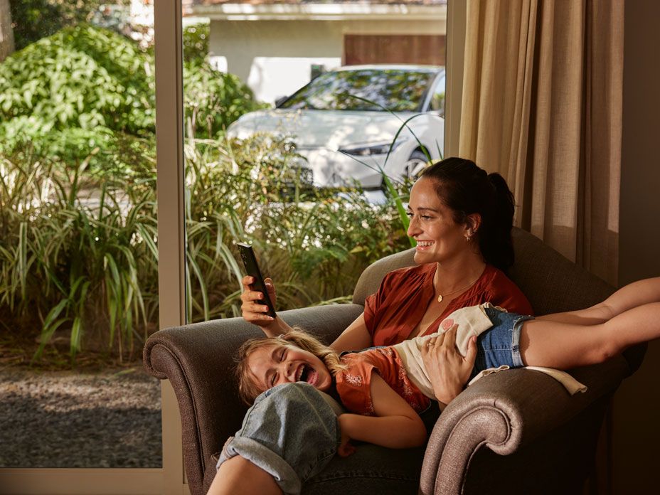 Eine Frau mit ihrer Tochter auf einem Sofa, die Frau blickt auf ihr Smartphone