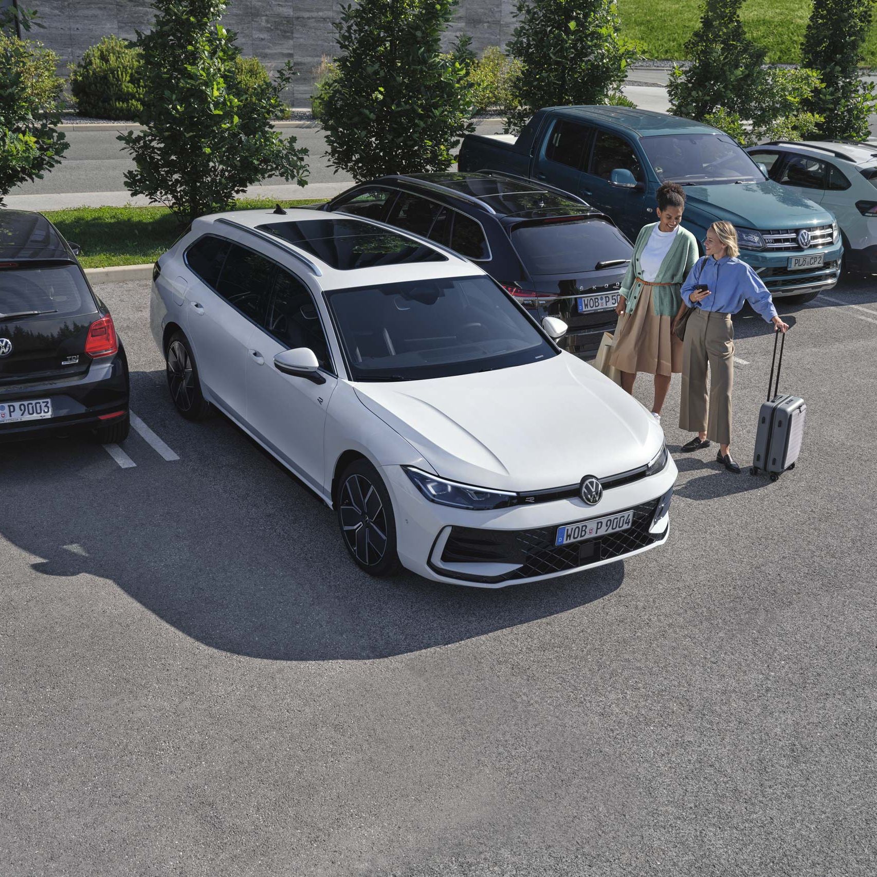 Duas mulheres do lado de fora do VW Passat branco, que estaciona por elas utilizando o sistema opcional Park Assist Plus. Uma mulher segura o seu smartphone na mão.