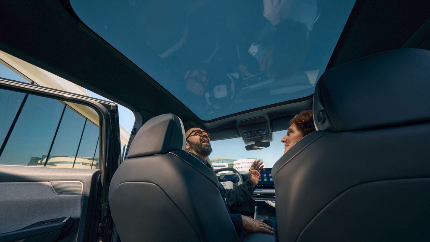 Um homem sentado no banco do condutor de um VW ID. Cross a olhar sorridente pelo teto de abrir panorâmico aberto.