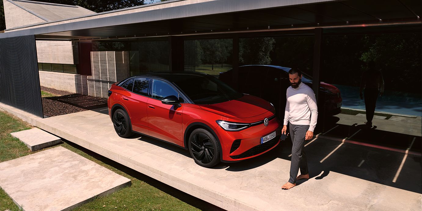 VW ID.5 GTX vermelho visto de dianteira na diagonal num carport moderno, um homem caminha à frente do capot