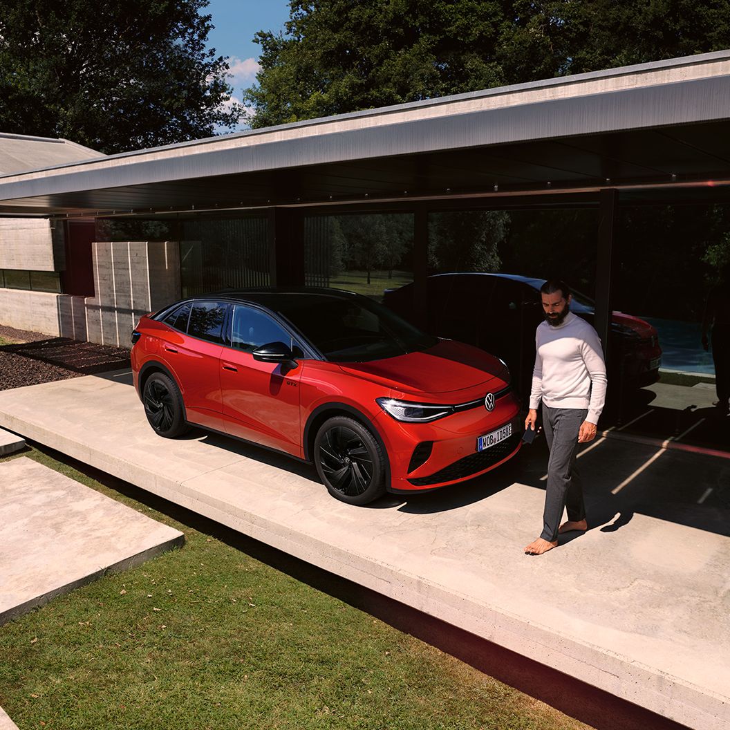 VW ID.5 GTX vermelho visto de dianteira na diagonal num carport moderno, um homem caminha à frente do capot