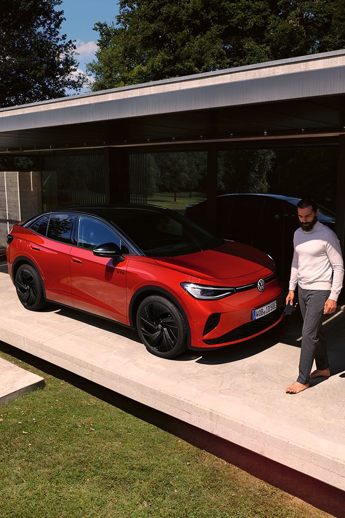VW ID.5 GTX vermelho visto de dianteira na diagonal num carport moderno, um homem caminha à frente do capot
