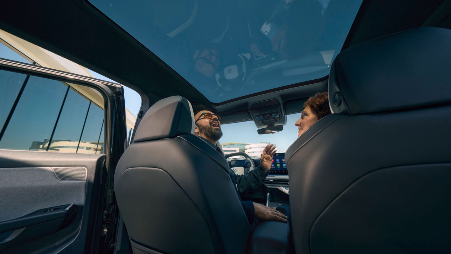 Um homem sentado no banco do condutor de um VW ID. Cross a olhar sorridente pelo teto de abrir panorâmico aberto.