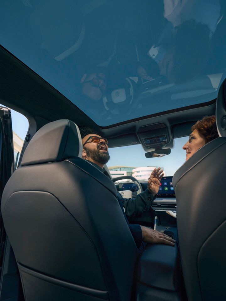 Um homem sentado no banco do condutor de um VW ID. Cross a olhar sorridente pelo teto de abrir panorâmico aberto.