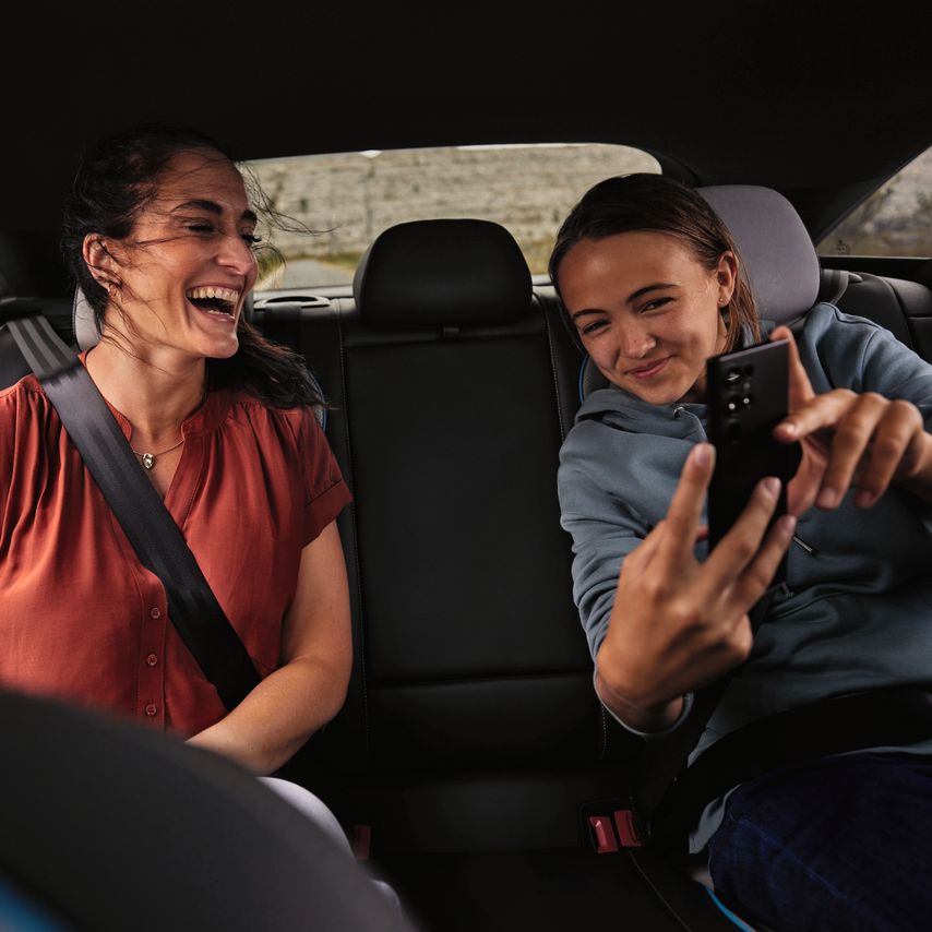 Duas pessoas sentadas no banco de trás de um Volkswagen. Uma delas segura um smartphone.