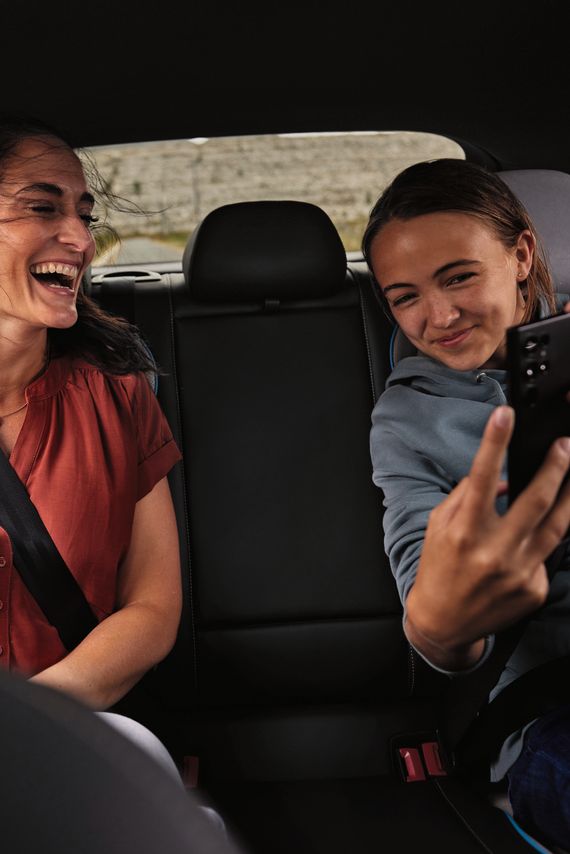 Duas pessoas sentadas no banco de trás de um Volkswagen. Uma delas segura um smartphone.