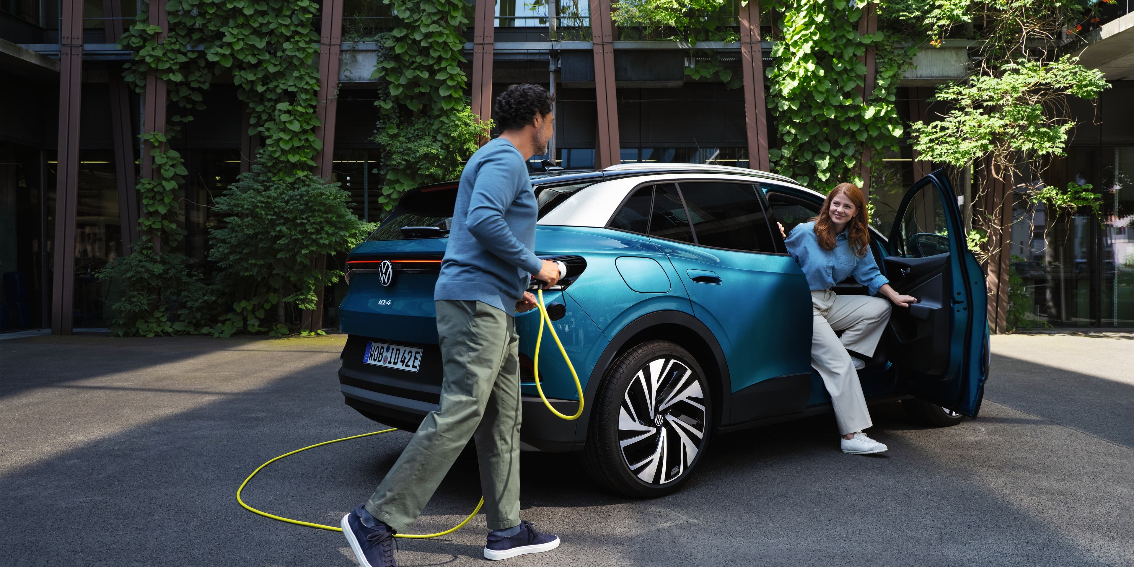 Volkswagen ID4 a carregar e duas pessoas, uma a mexer no carregador e outra a sair do veículo