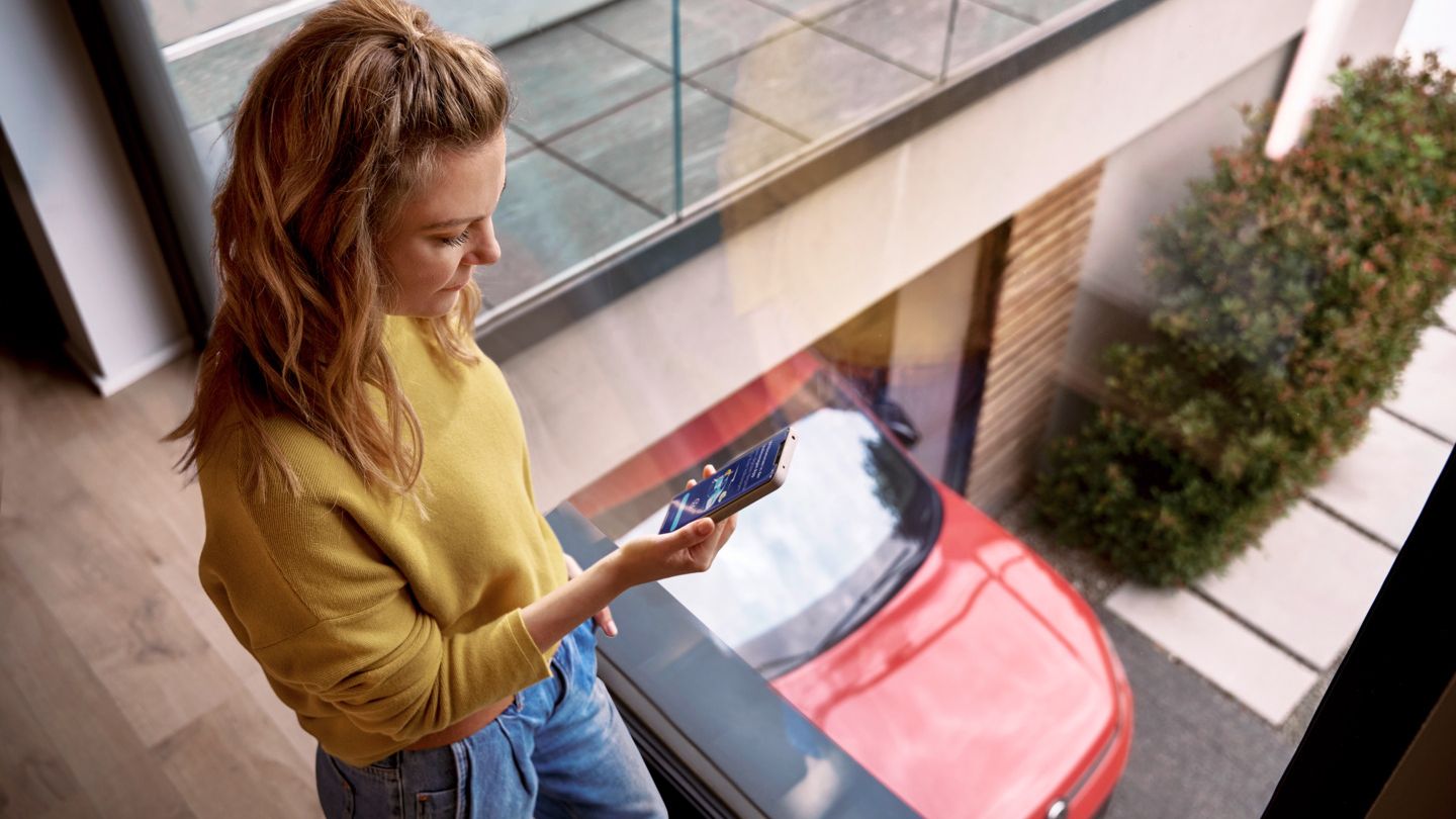 Frau schaut zu Hause auf ihr Smartphone, während ihr Tiguan in der Einfahrt geparkt ist.